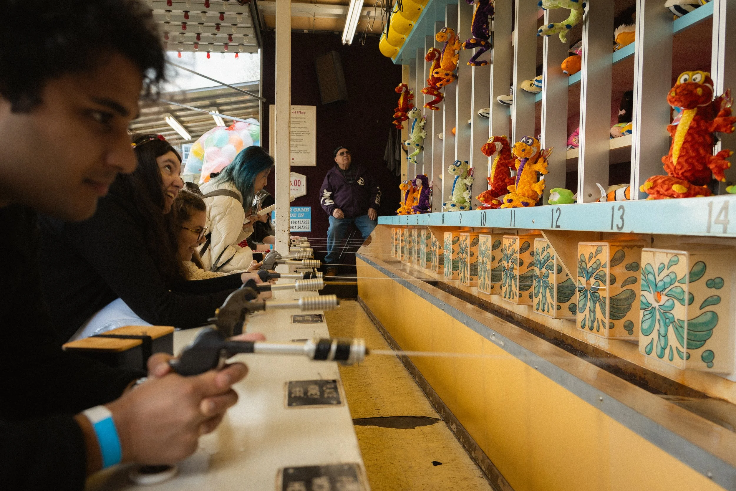 People playing a skee-ball game at an arcade with plush dragon toys on the wall.