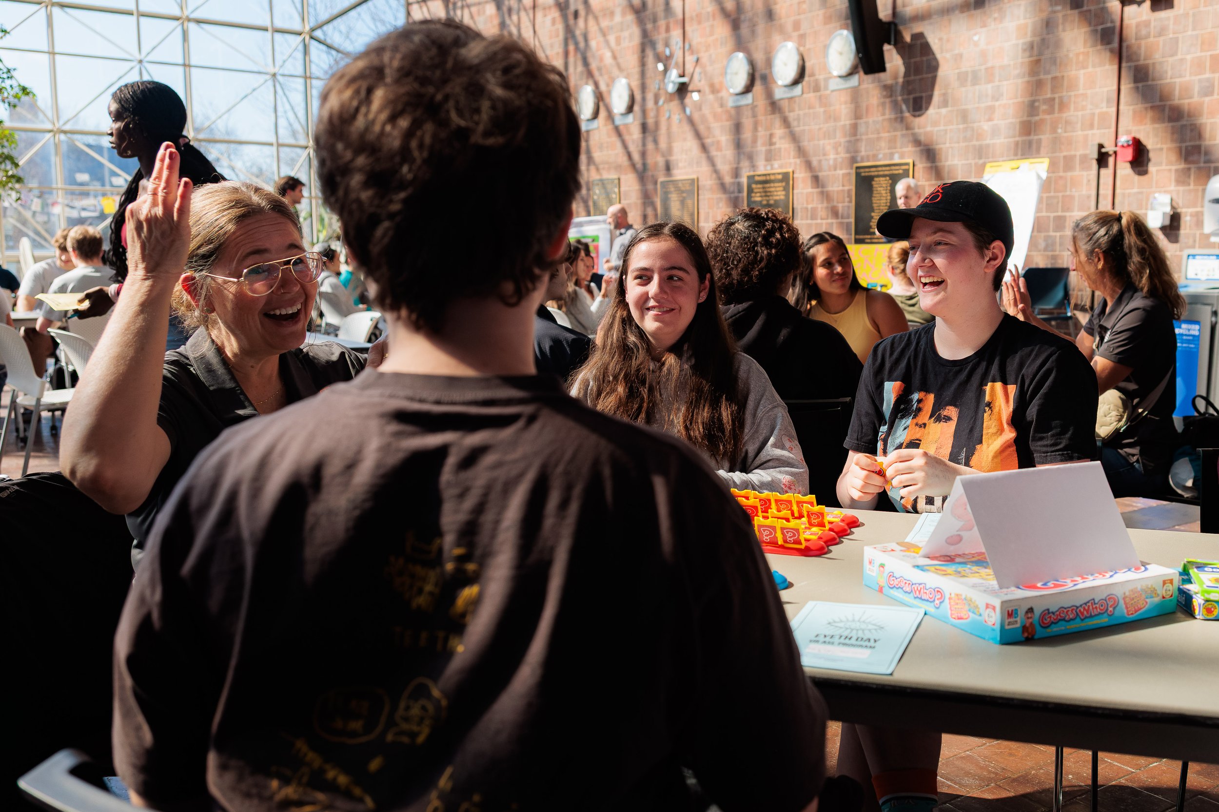 People gathered around a table at an indoor event, engaged in conversation, with board game boxes in front of them.