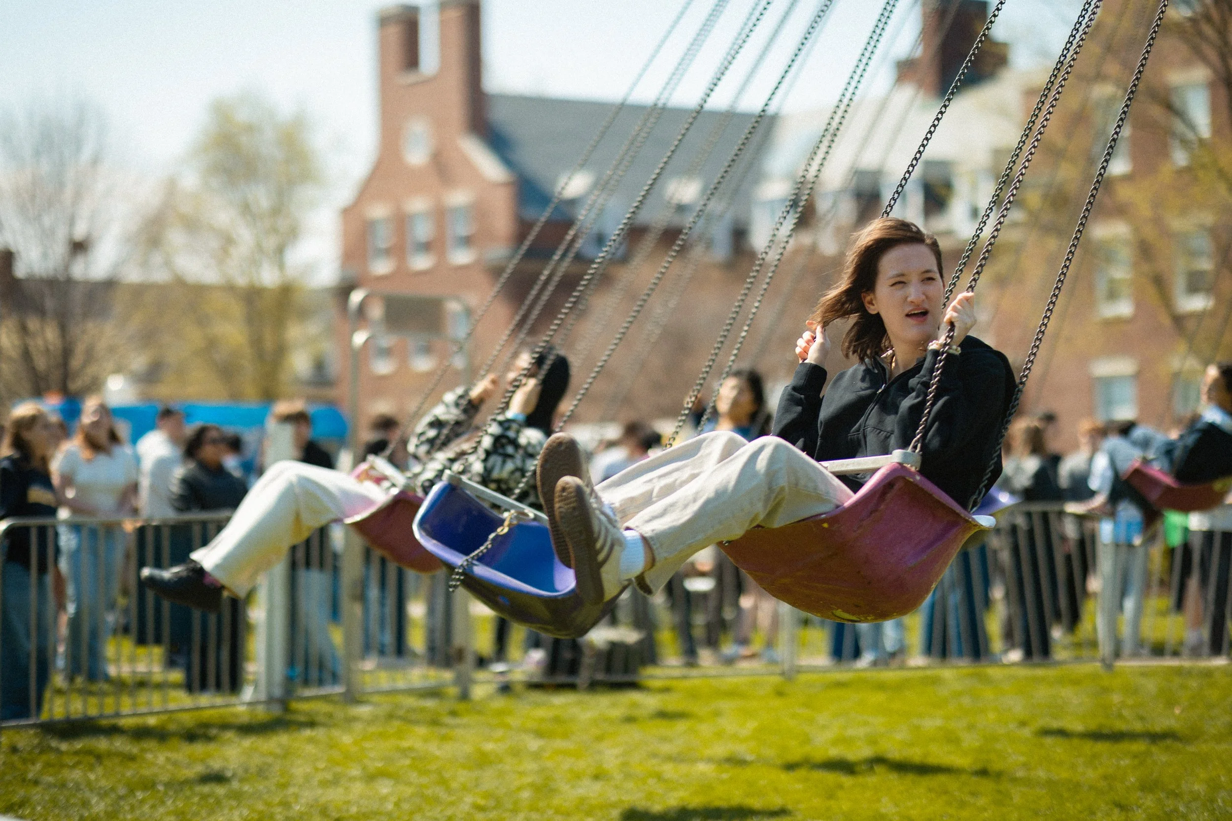 A girl on a swing ride at an outdoor amusement park, with other people and buildings in the background.