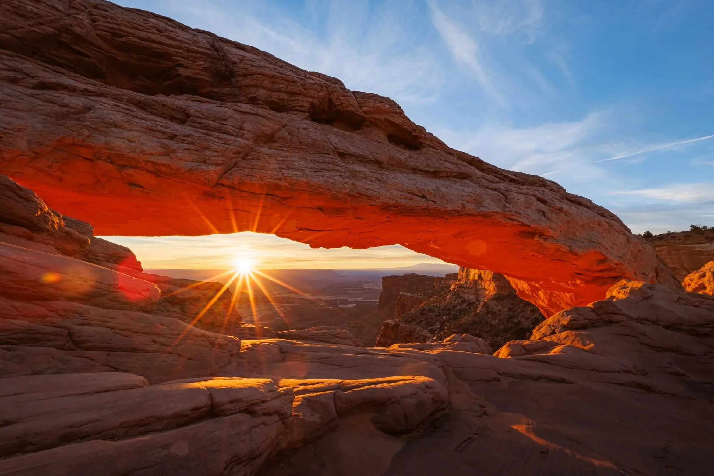 Sunset through a natural rock arch in a desert landscape.