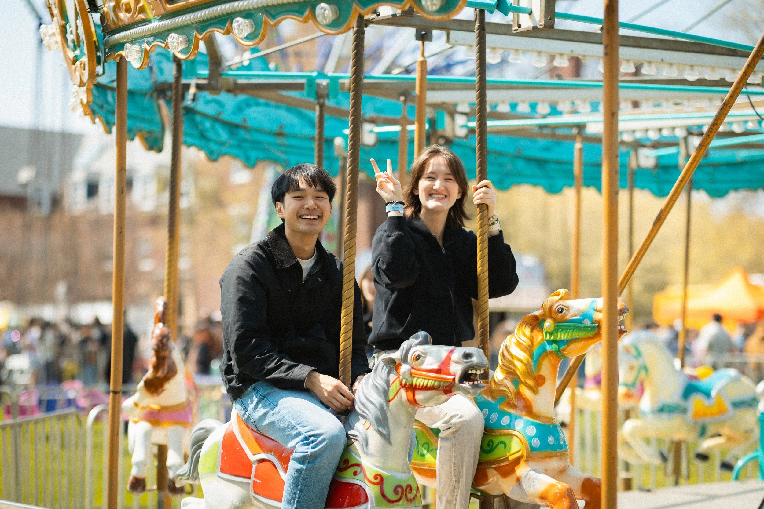 Two people riding a carousel horse at an amusement park, smiling and enjoying the ride.