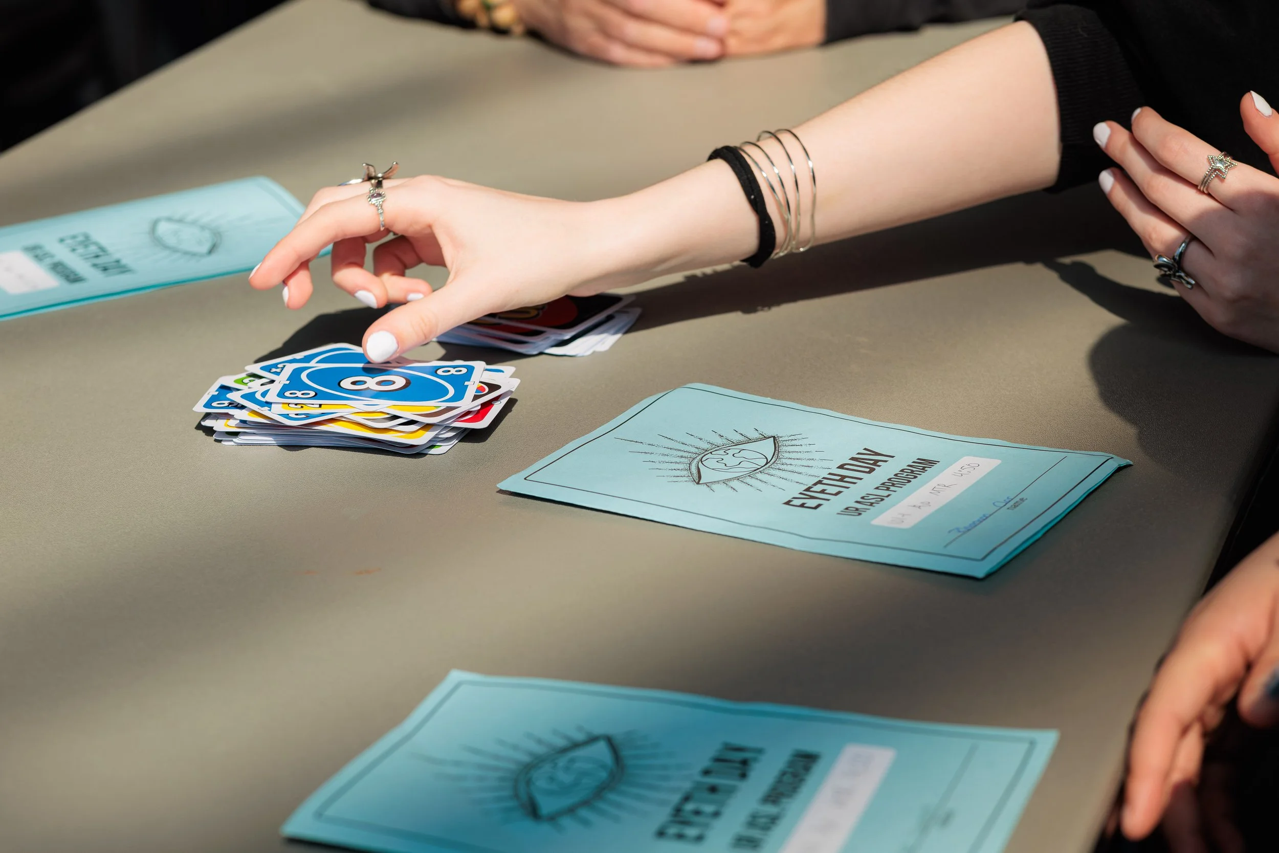 People playing cards at a table with a blue informational booklet and a deck of UNO cards.