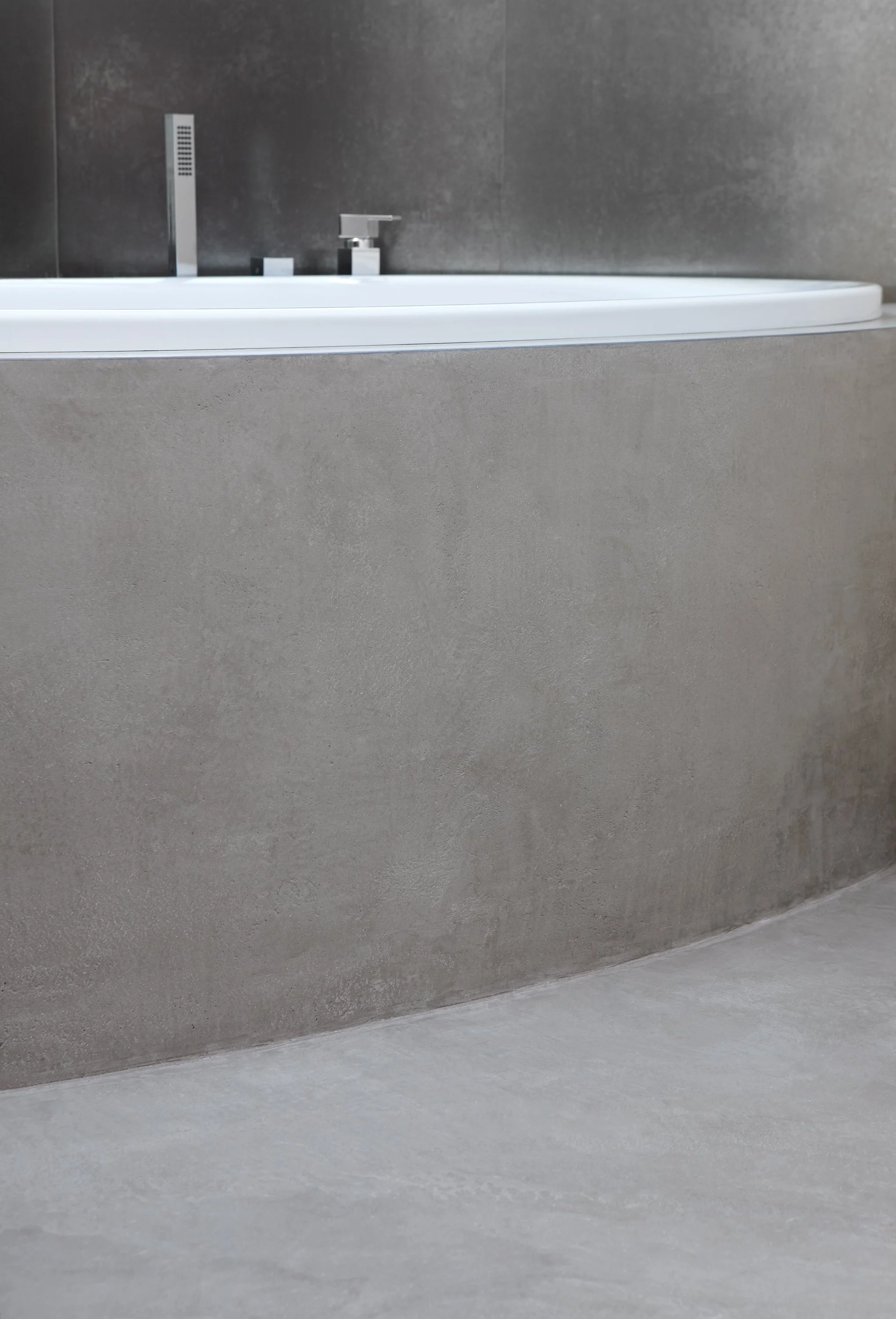 Close-up photo of a modern bathtub with a gray textured concrete wall in the background.