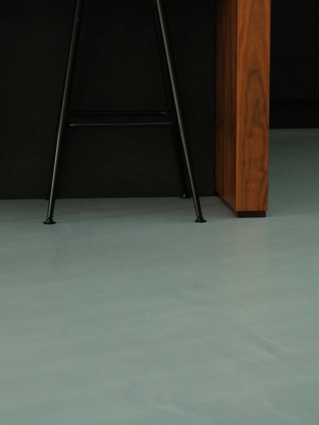 Part of a black wall or furniture, a black metal chair with thin legs, and a wooden piece of furniture or wall on the right side.