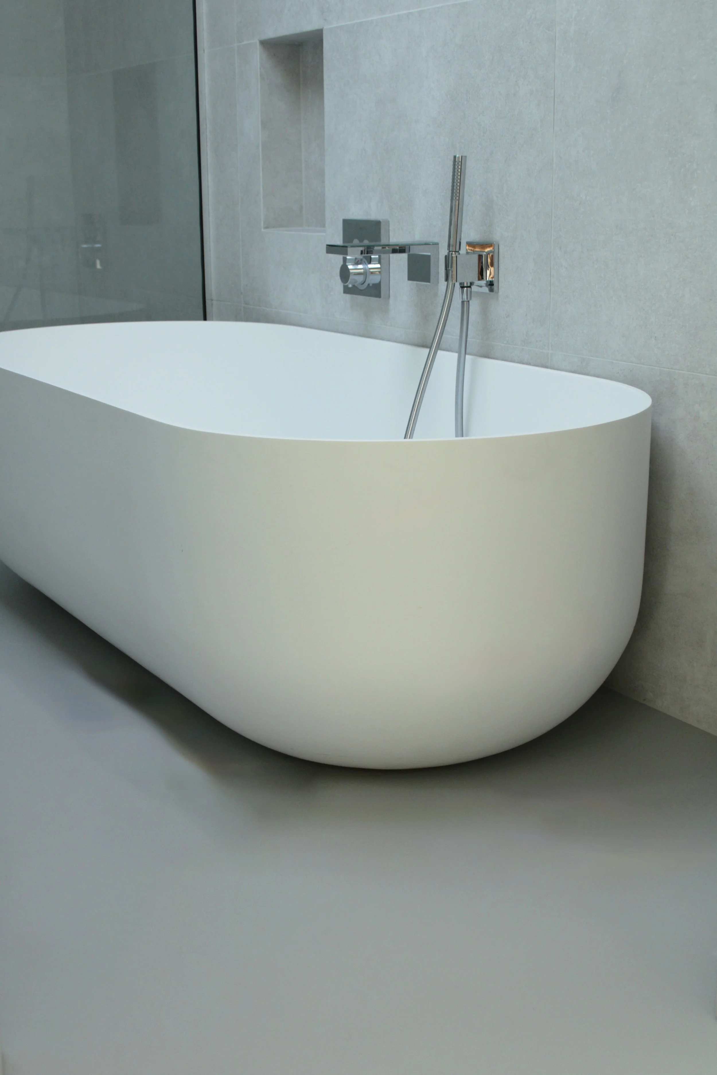 Modern bathtub with wall-mounted chrome faucet and handheld showerhead in a minimalist bathroom.