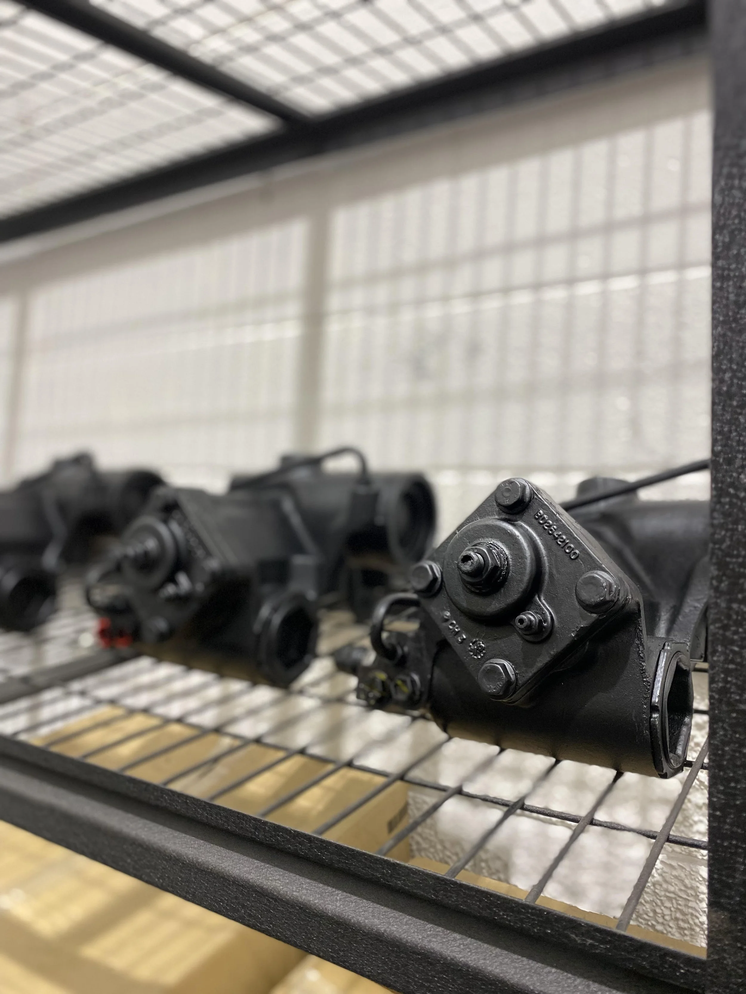 Black mechanical parts, possibly machinery or engine components, placed on a metal grating surface with a blurred background.