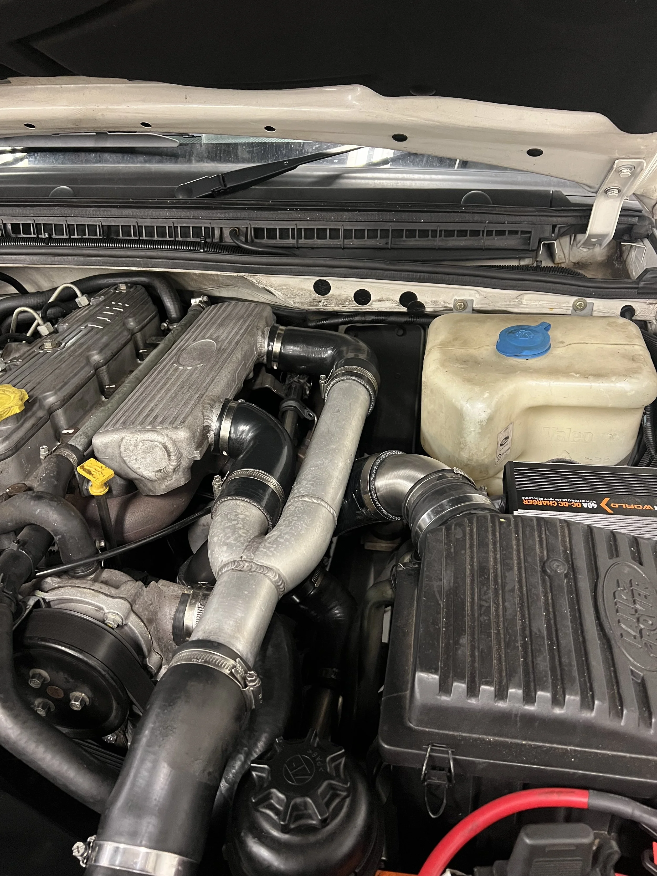 Close-up view of a car engine bay showing various engine components, piping, and a coolant reservoir.