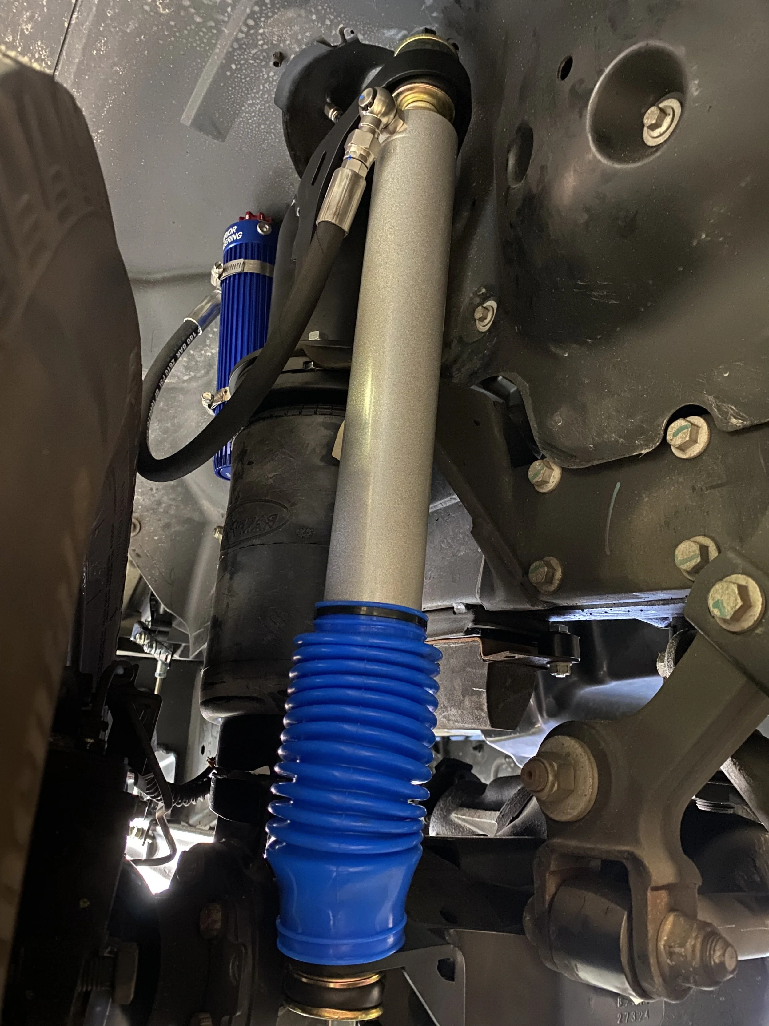 Close-up view of a vehicle's suspension system, including a blue coil spring, shock absorber, and various other suspension components.