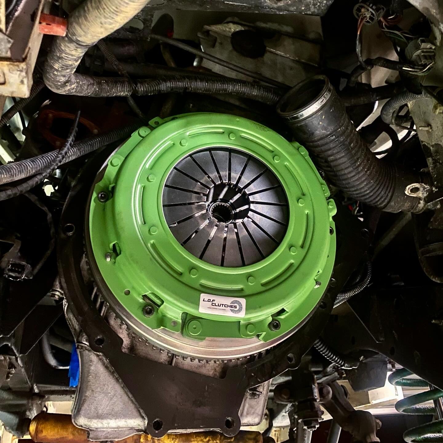Close-up of an automotive clutch assembly with a new bright green clutch cover installed inside the engine bay of a vehicle.