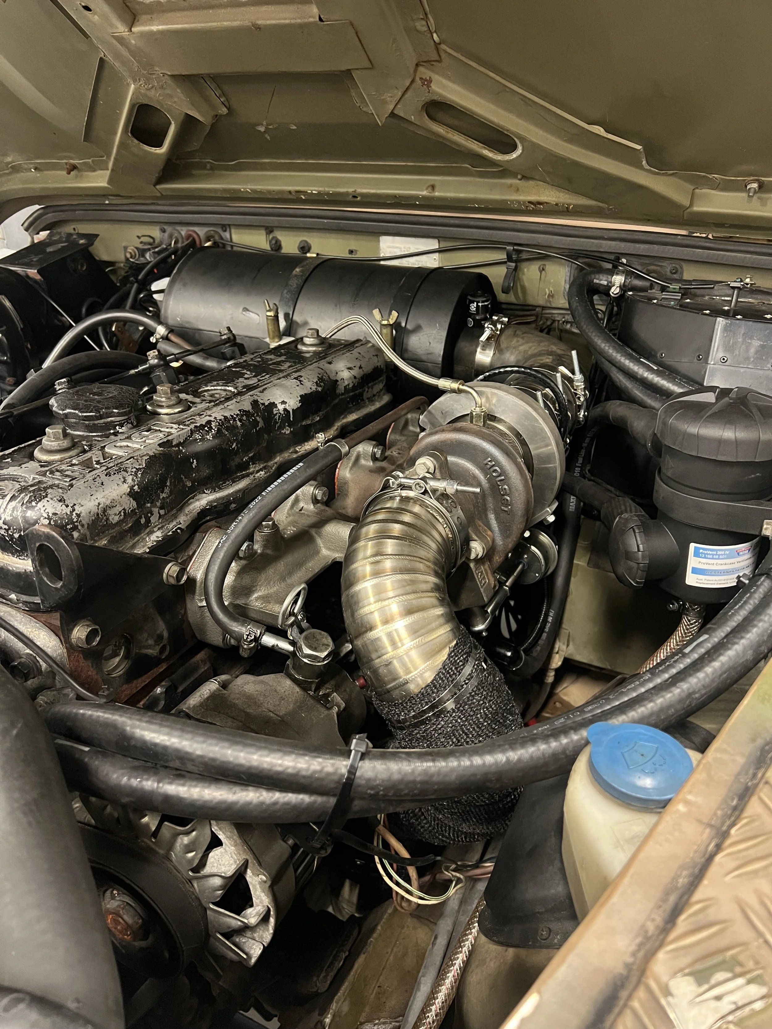 Close-up view of a vehicle engine showing various components, pipes, and hoses under the hood.
