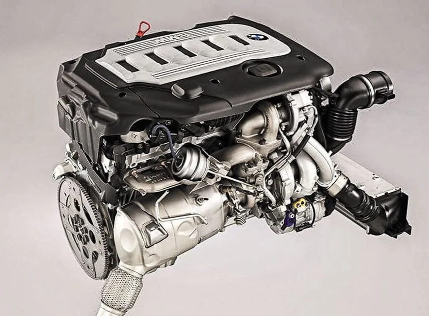 A BMW engine with various metallic parts, black and silver components, and a black plastic cover on top.