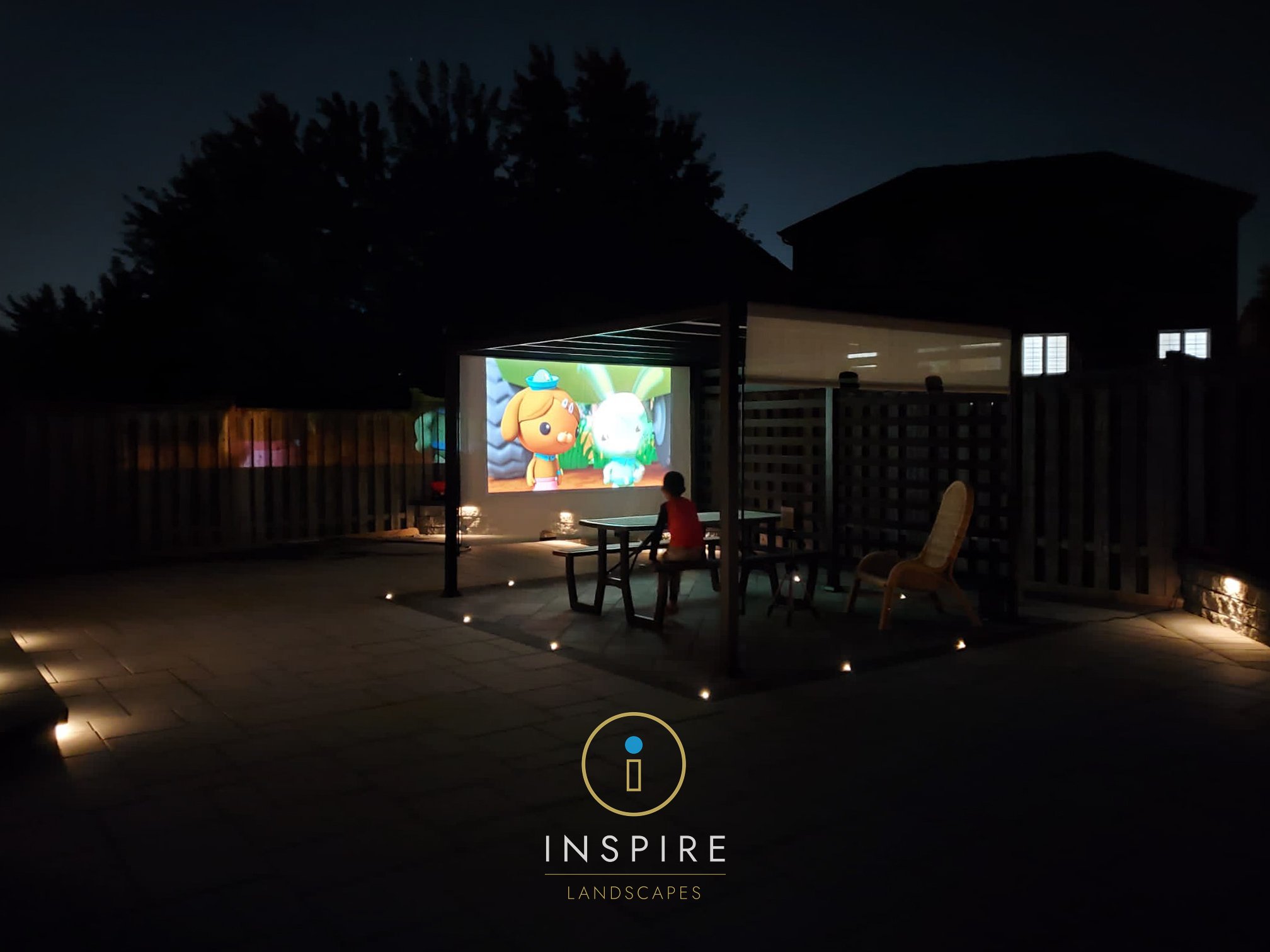 Sleek modern backyard installed with Unilock Beacon Hill in Opal and Granite Fusion mixed colorway paired with aluminum pergola and privacy screen used for outdoor movie screen with full outdoor ambient lighting