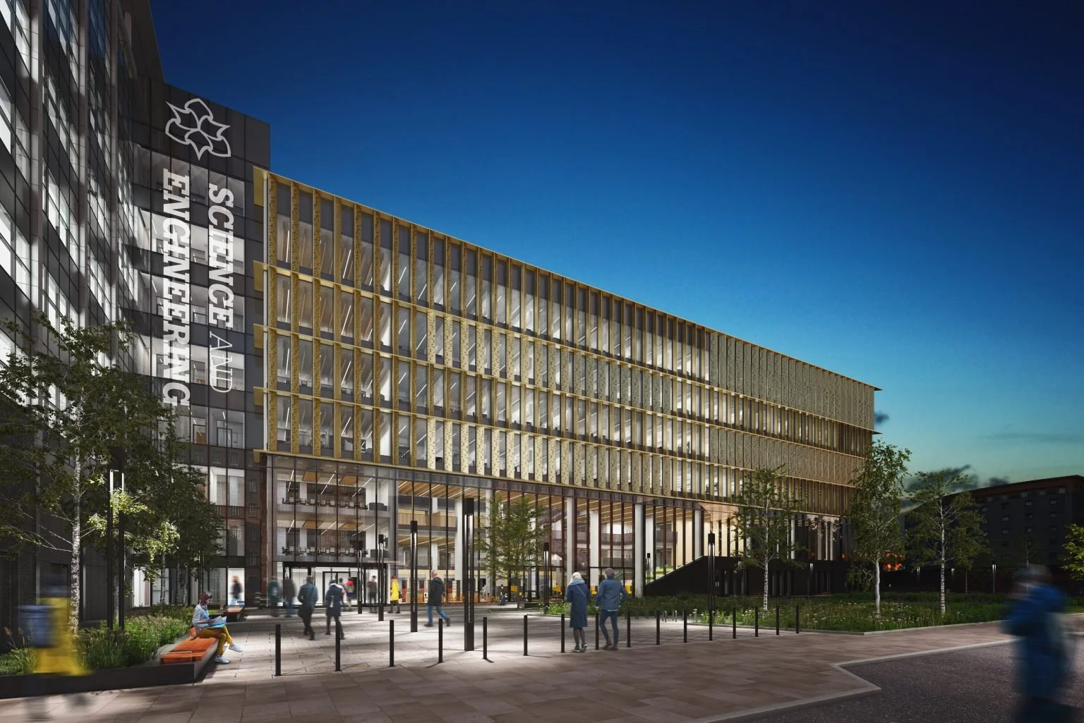 Nighttime view of a modern hospital building with glass exterior and wooden window frames, people walking and sitting outside, trees and street lamps in the foreground.