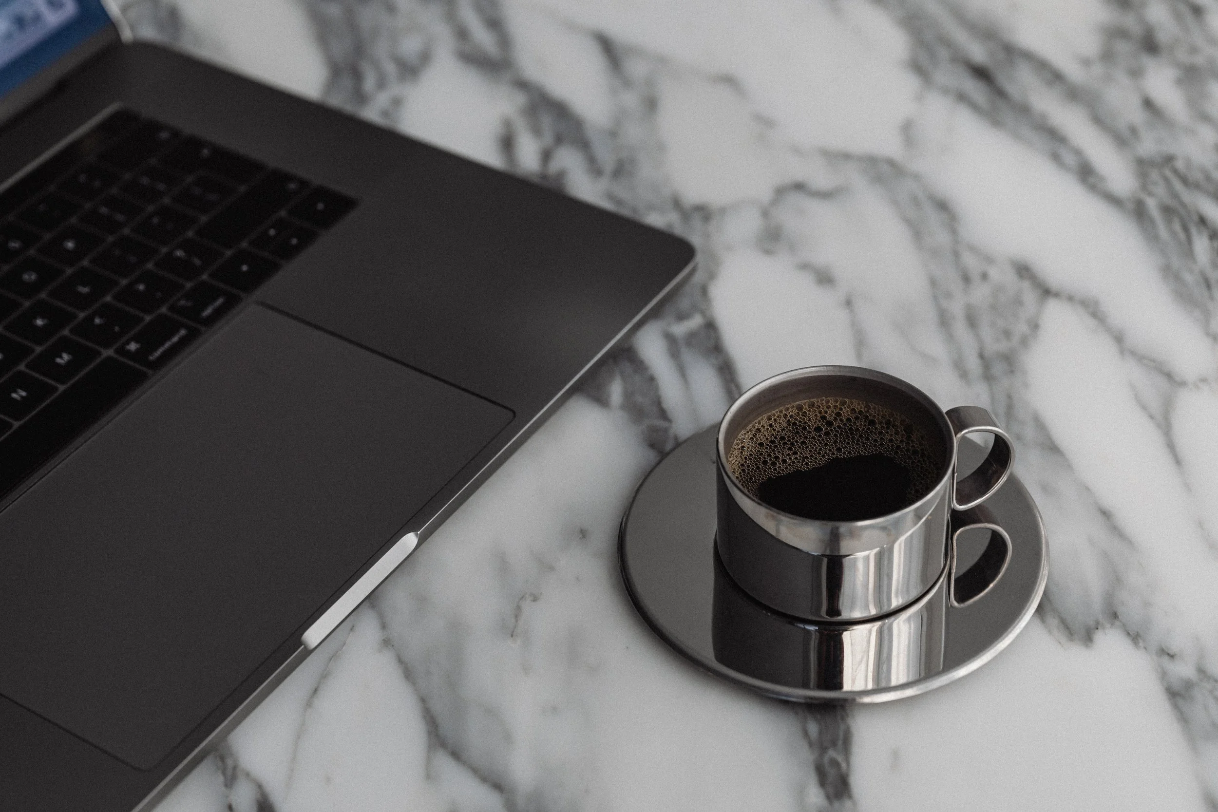 Laptop computer and a cup of black coffee on a marble countertop.