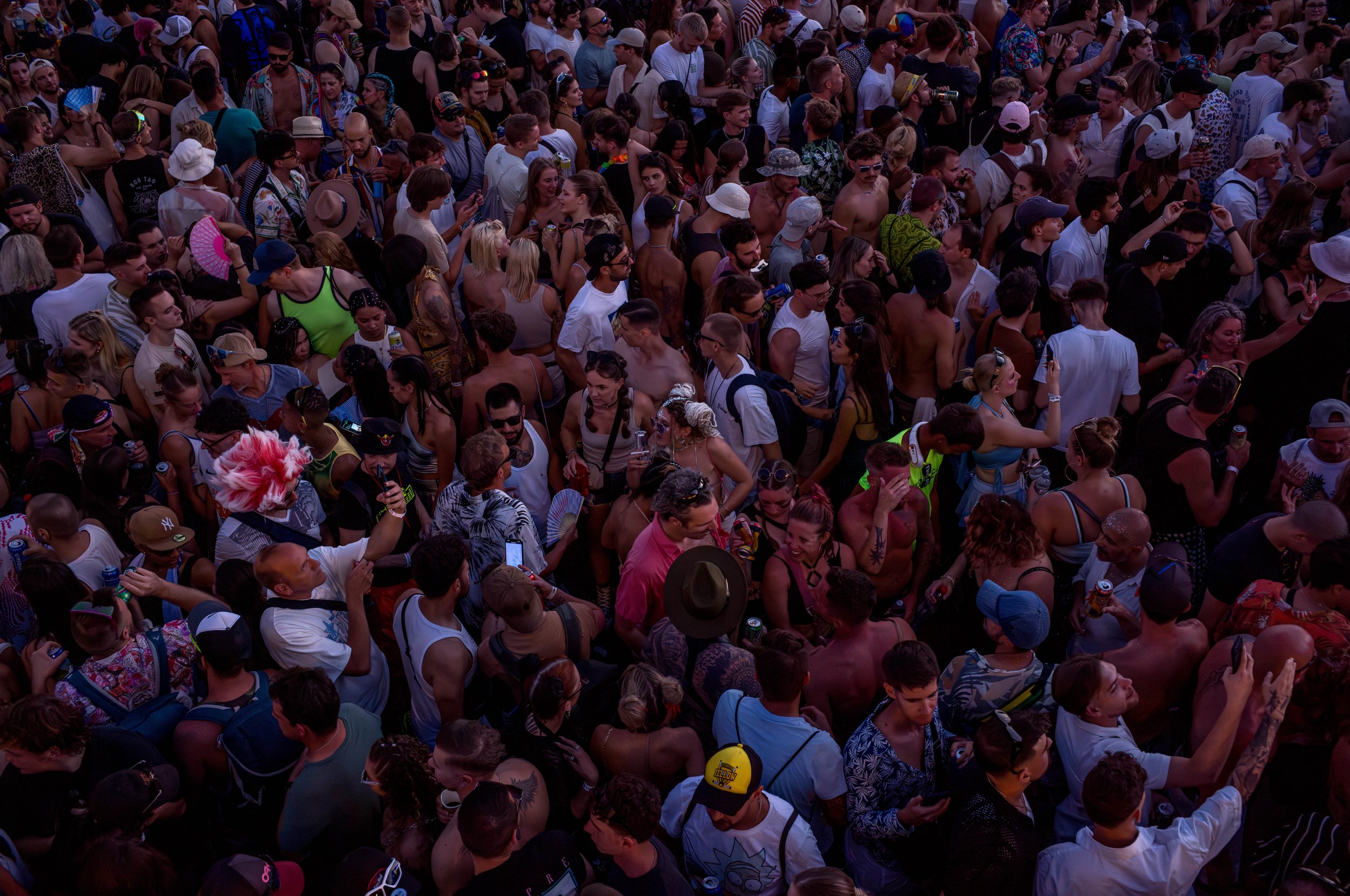 Menschenmenge bei einem Festival oder Event, viele tragen casual Kleidung, Hüte, Sonnenbrillen und verwenden Smartphones.