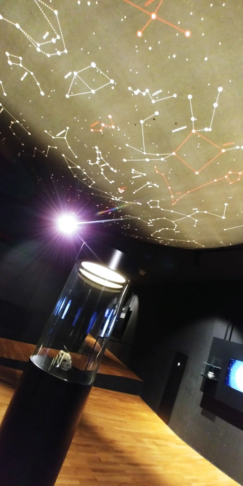 Celestial star map display on a ceiling, with a bright light in the museum or planetarium setting, a star model in a transparent case on a wooden table.