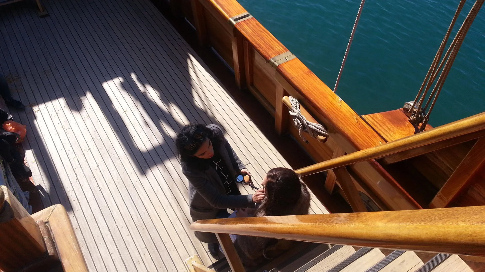 Two women exchanging a kiss on the deck of a boat, with water visible in the background and wooden railings surrounding them.