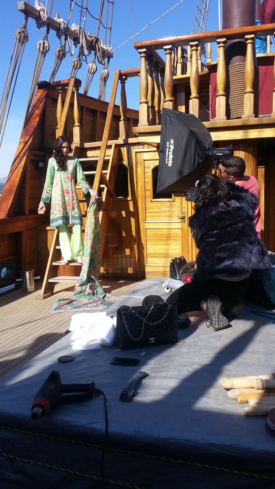 A photoshoot on a boat with a woman in a traditional outfit, a photographer, and an assistant, with photography equipment and props nearby.