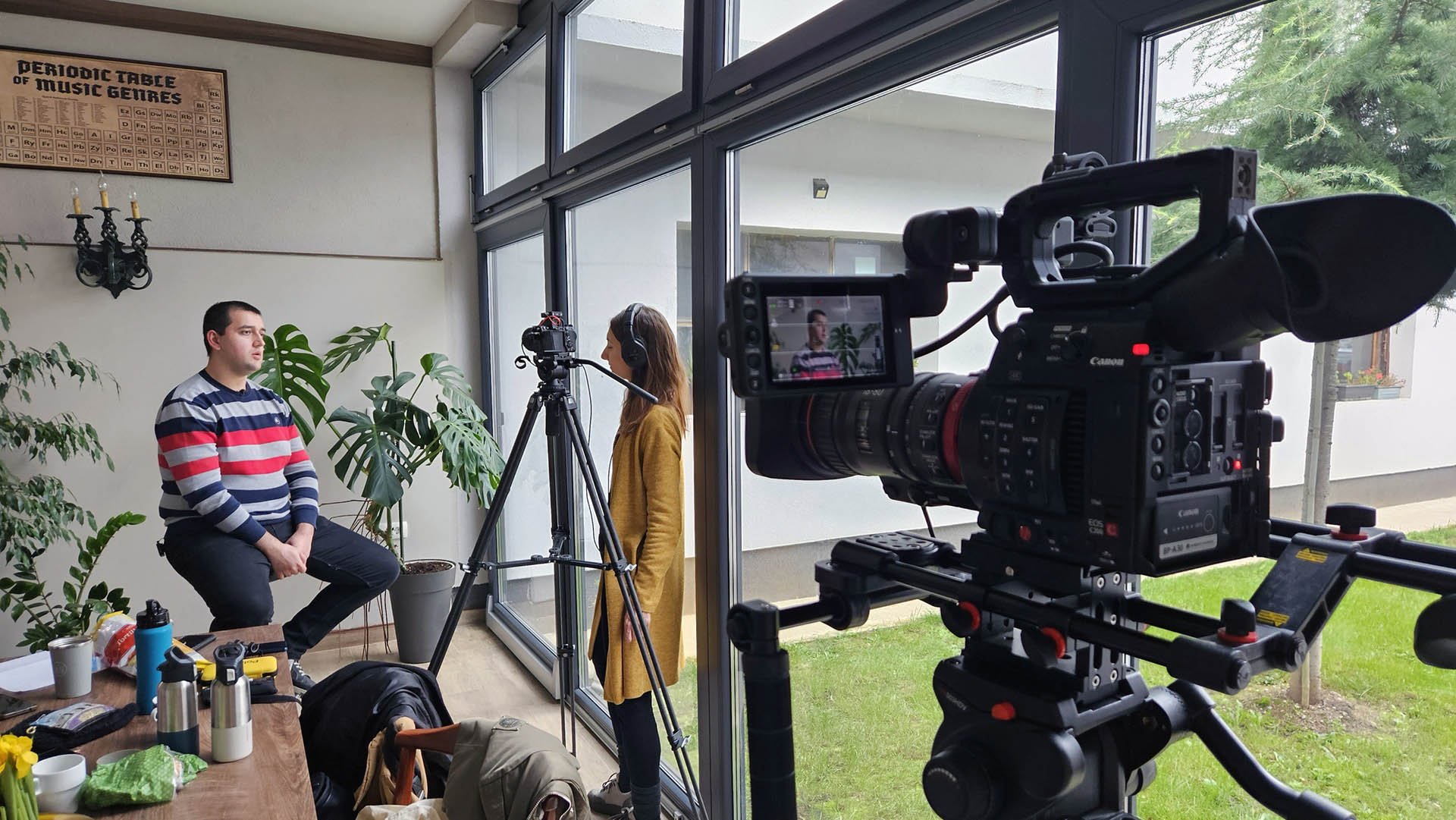 Multi-camera interview setup in an indoor glass-enclosed space with two cameramen filming a professional interview with lighting equipment.