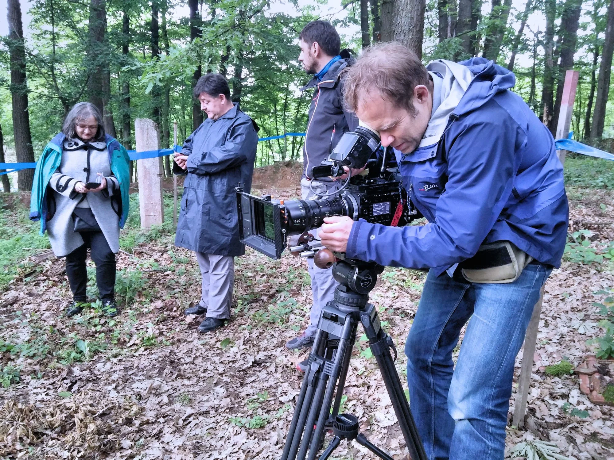 People working in a forest with a camera on a tripod, likely filming or photographing nature.