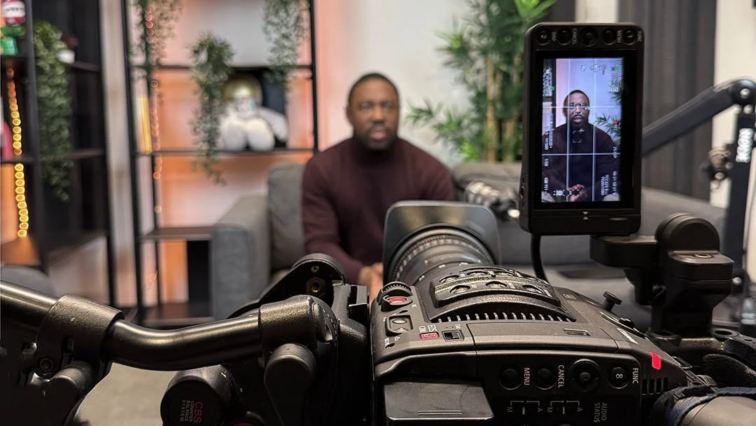 Podcast recording in a studio with a vertical camera setup, showing a focused speaker on the camera screen, microphones in the foreground, and the speaker visible in the blurred background.