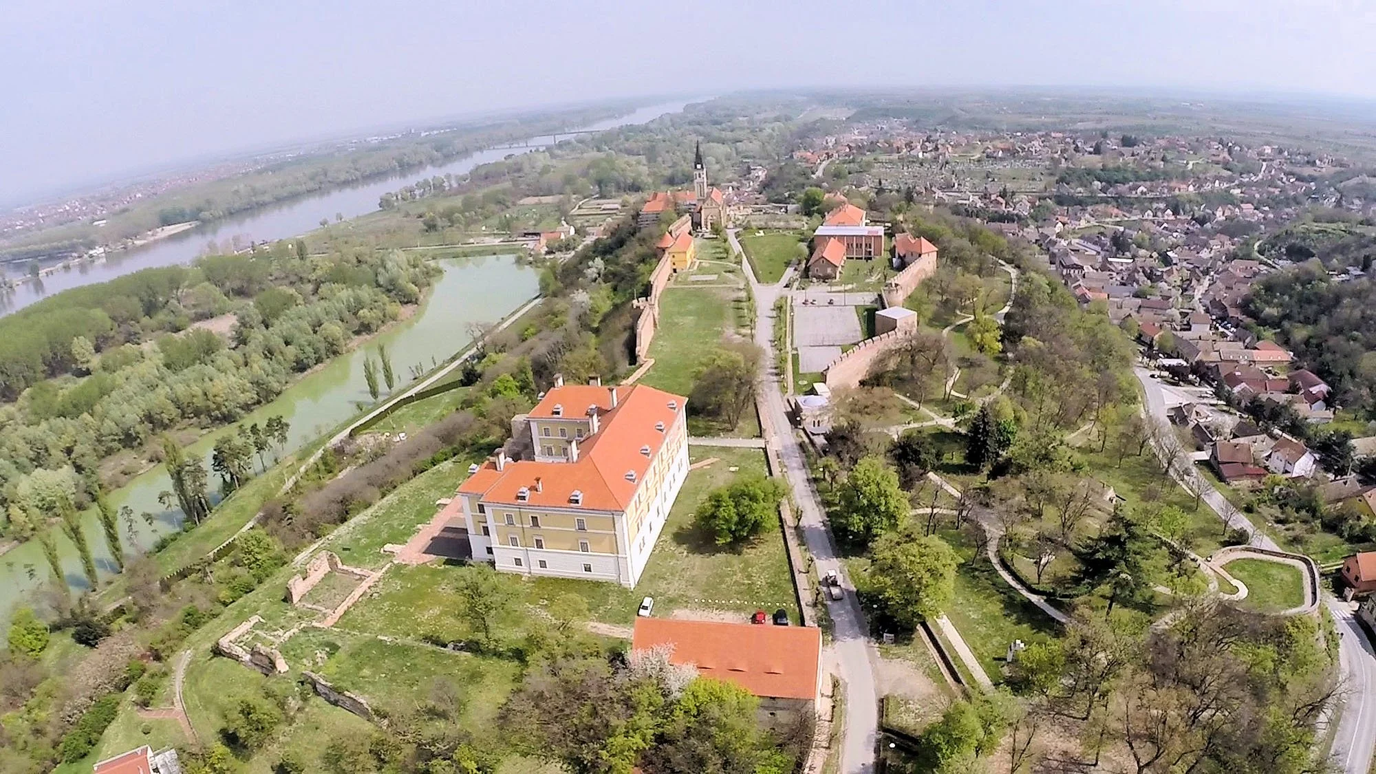 Aerial view of a historic fortress surrounded by a green landscape, a river, and a town with residential buildings and green spaces.
