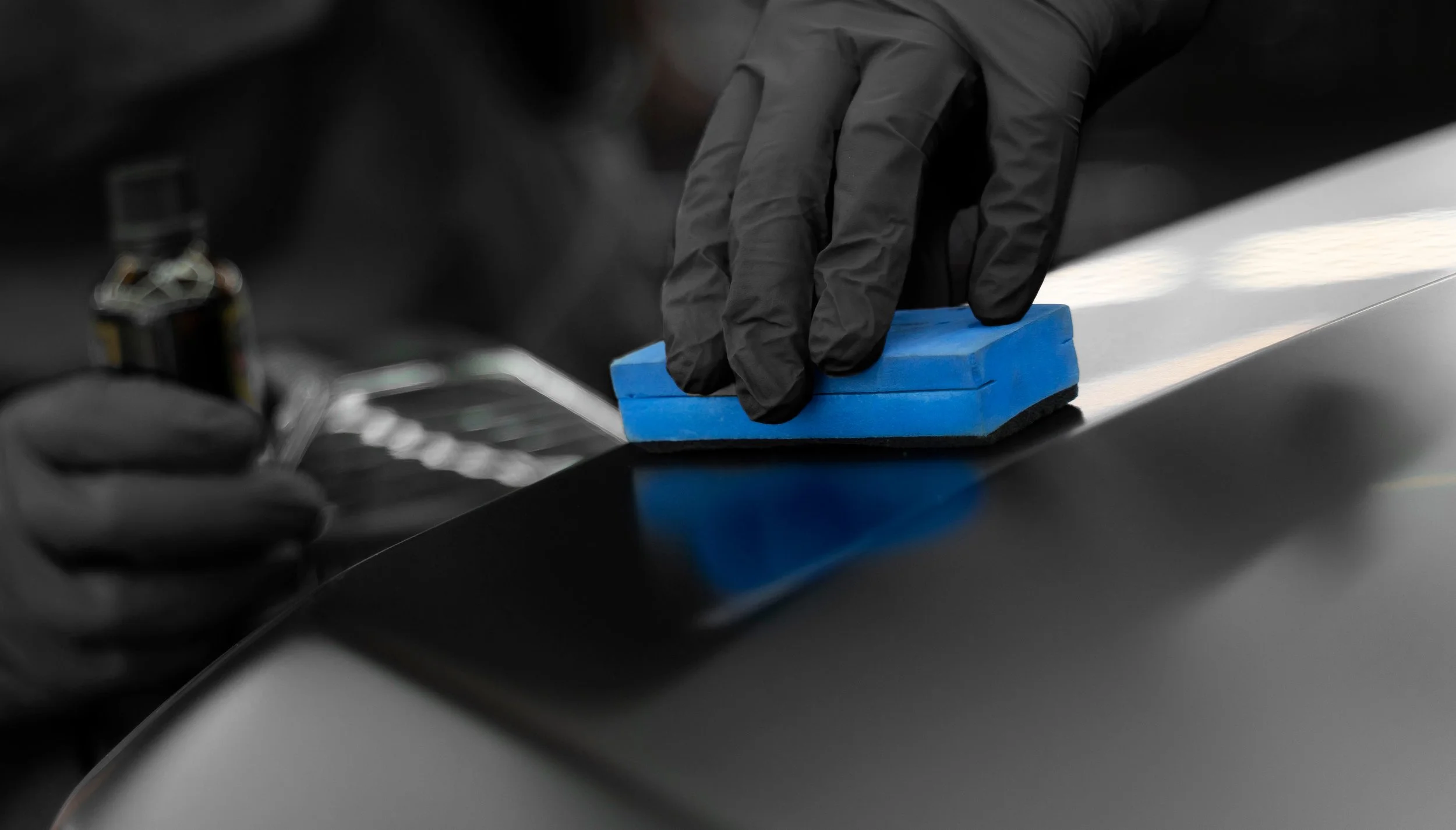 Ty applying a graphene infused ceramic coating to a black Audi hood using an applicator block.