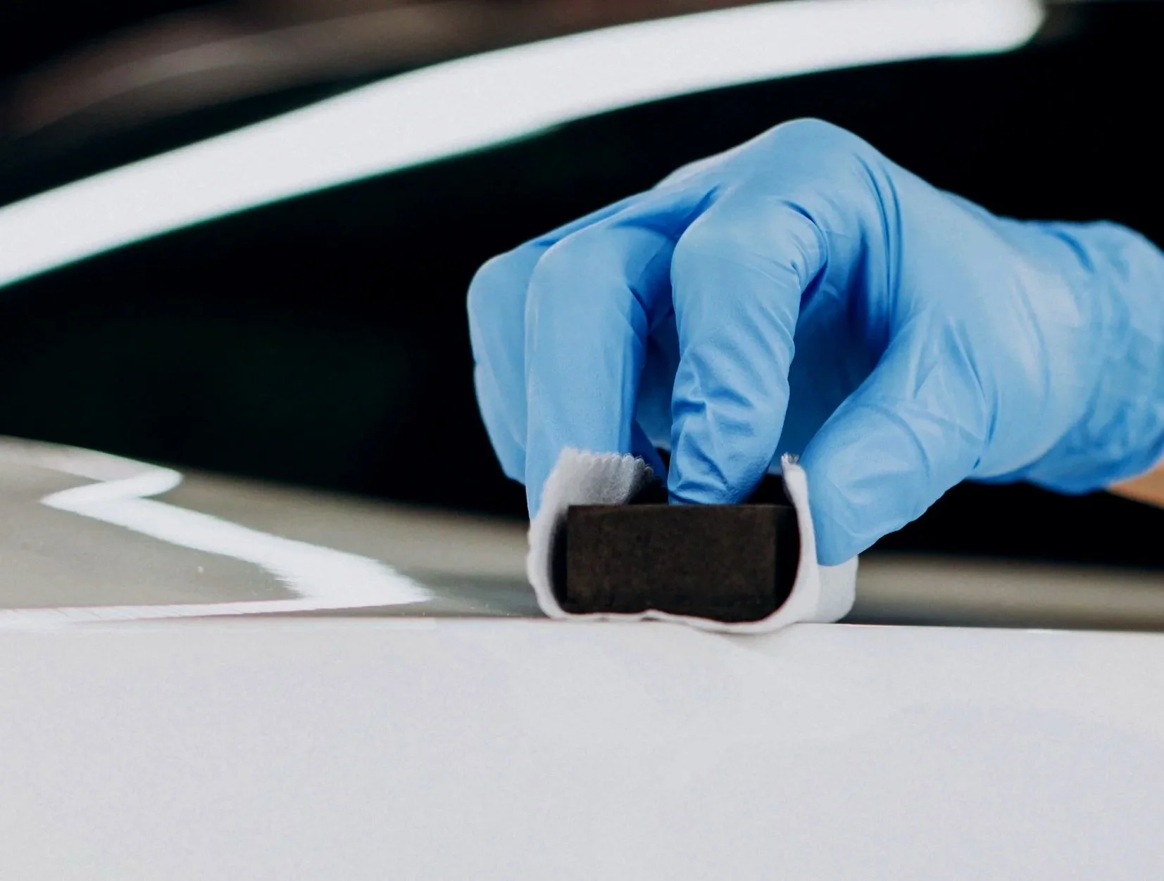 White BMW 3-Series receiving application of a ceramic coating using an applicator block and cloth.