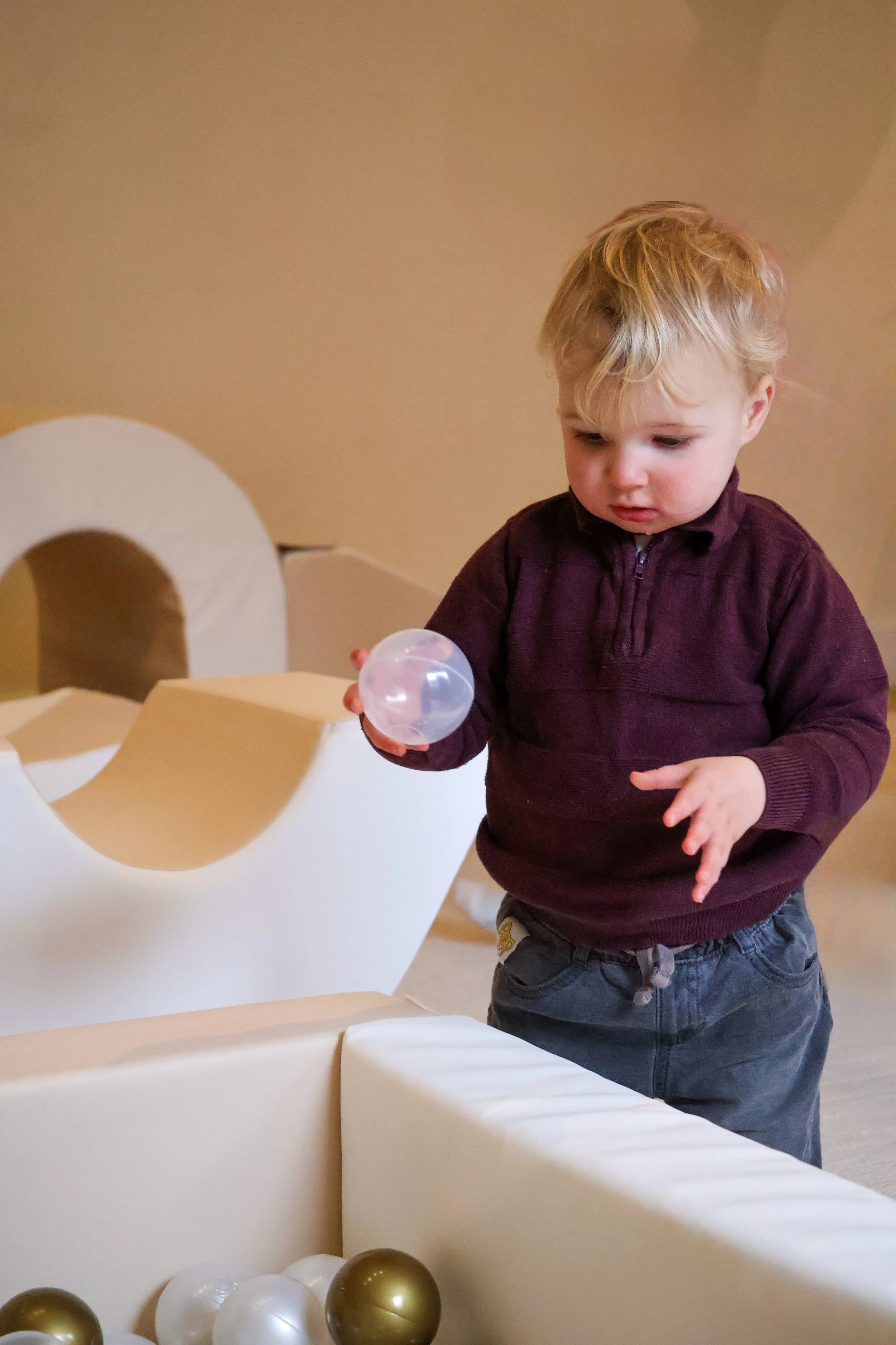 Toddler holding a ball in a play area with white and gold balls.