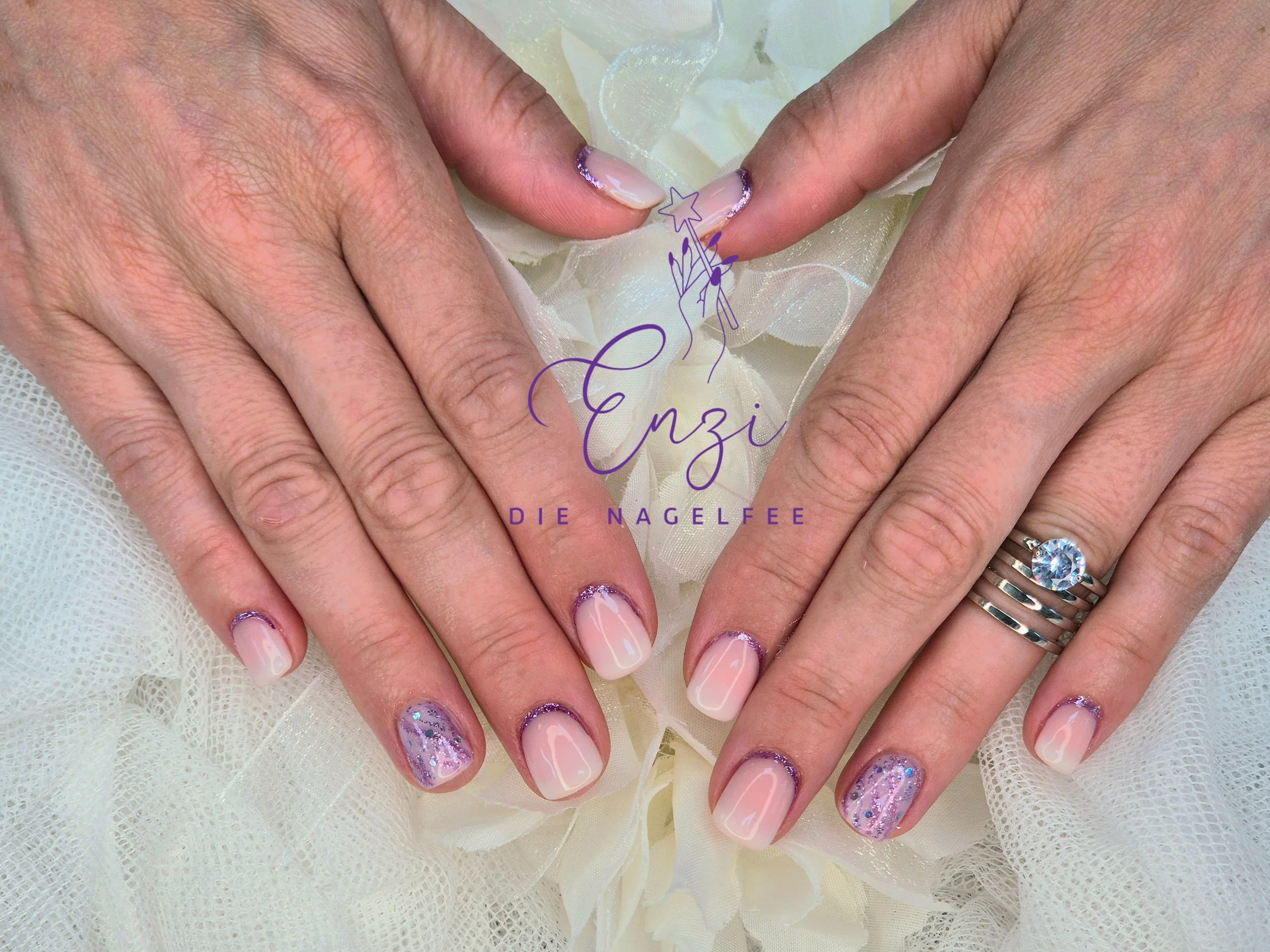 Hände mit Nageldesigns, darunter eine Hand mit einem großen Verlobungsring, auf cremefarbenem Stoff, mit einem handschriftlichen Text und einem Logo in der Mitte.