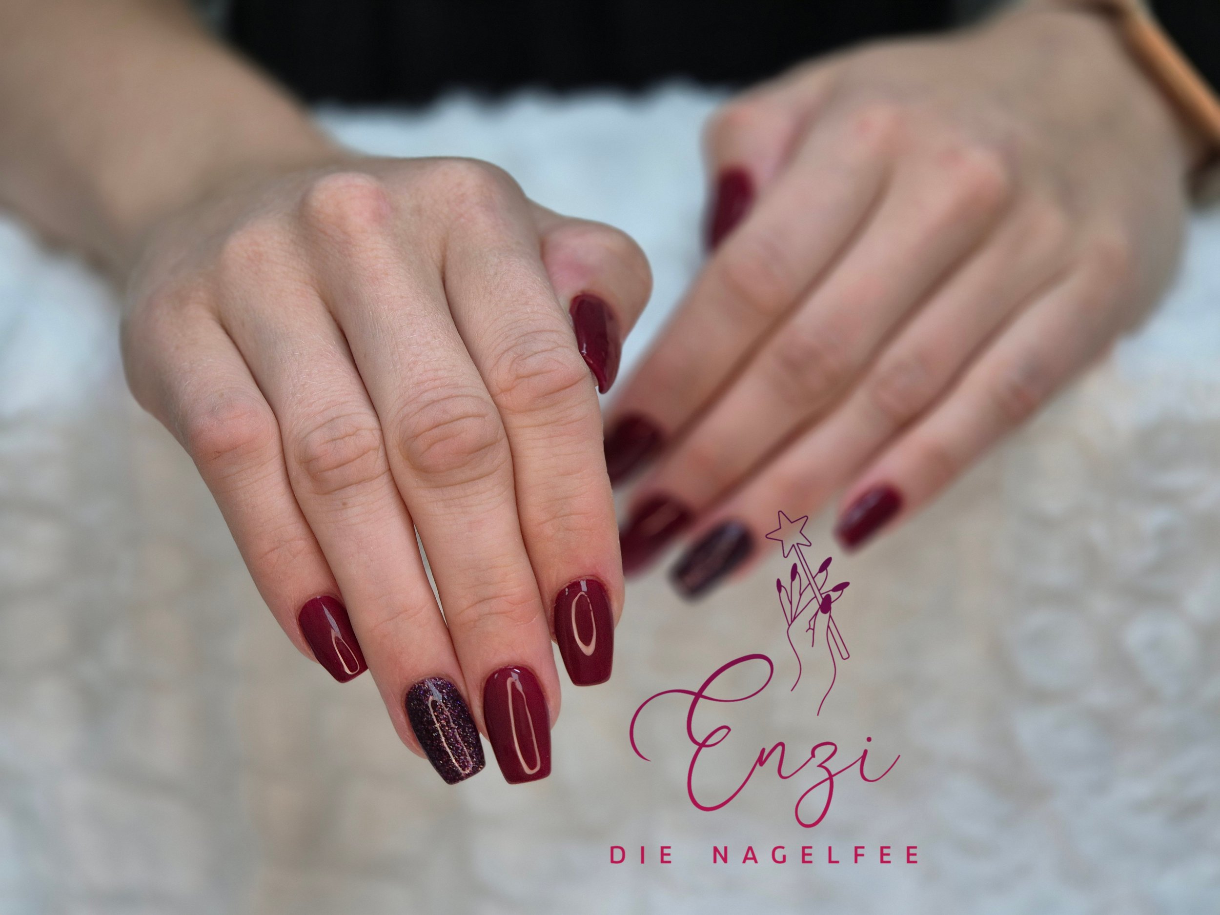 Nägel mit dunklem rotem und glitzerndem Nagellack, auf einem weißen Untergrund, mit einem Logo und Text darunter.
