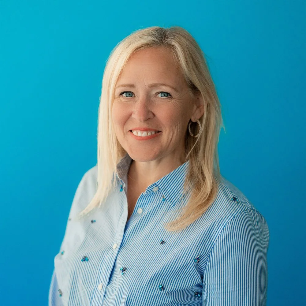 Smiling woman with blonde hair standing against a blue background.