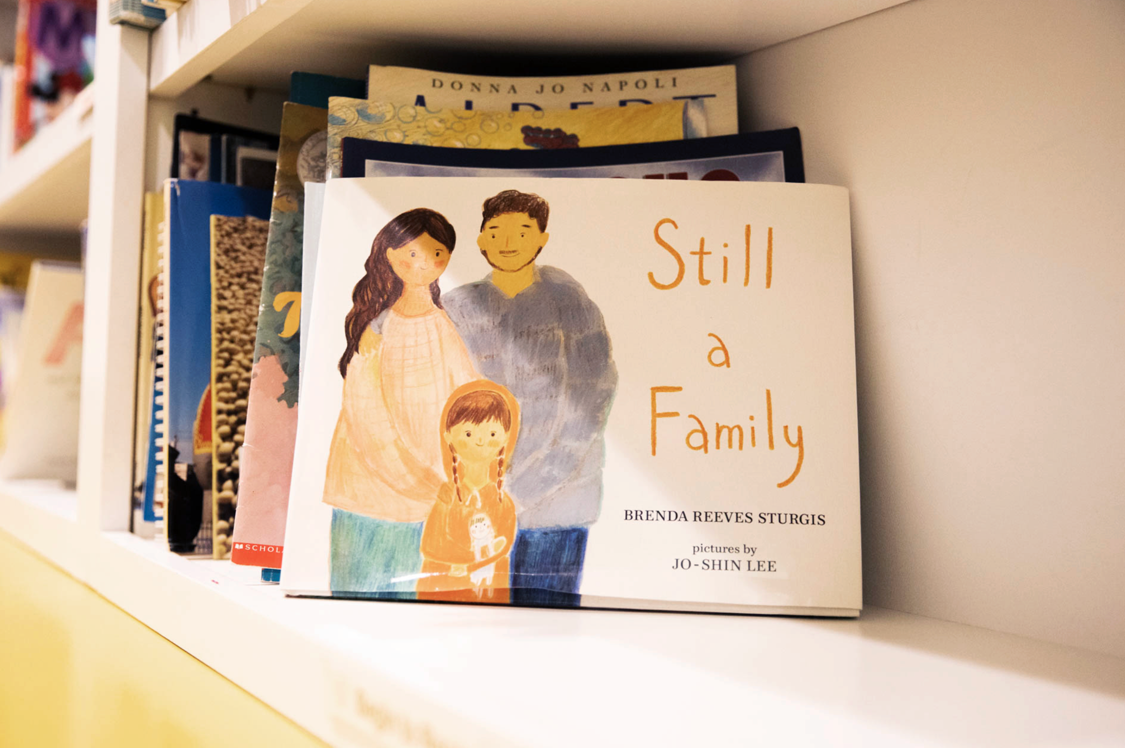Bookshelf with the book 'Still a Family' featuring an illustration of a family on the cover.