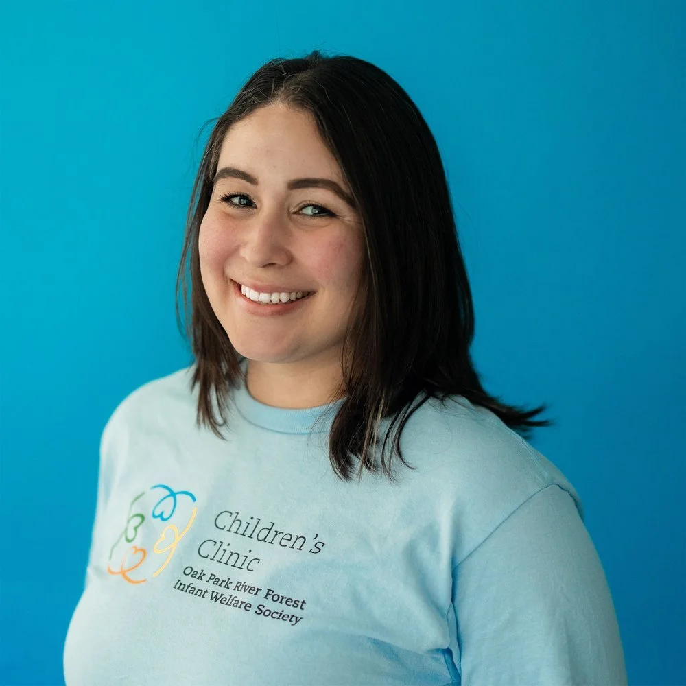 Person wearing a light blue t-shirt with 'Children's Clinic, Oak Park River Forest, Infant Welfare Society' printed on it, standing against a blue background.