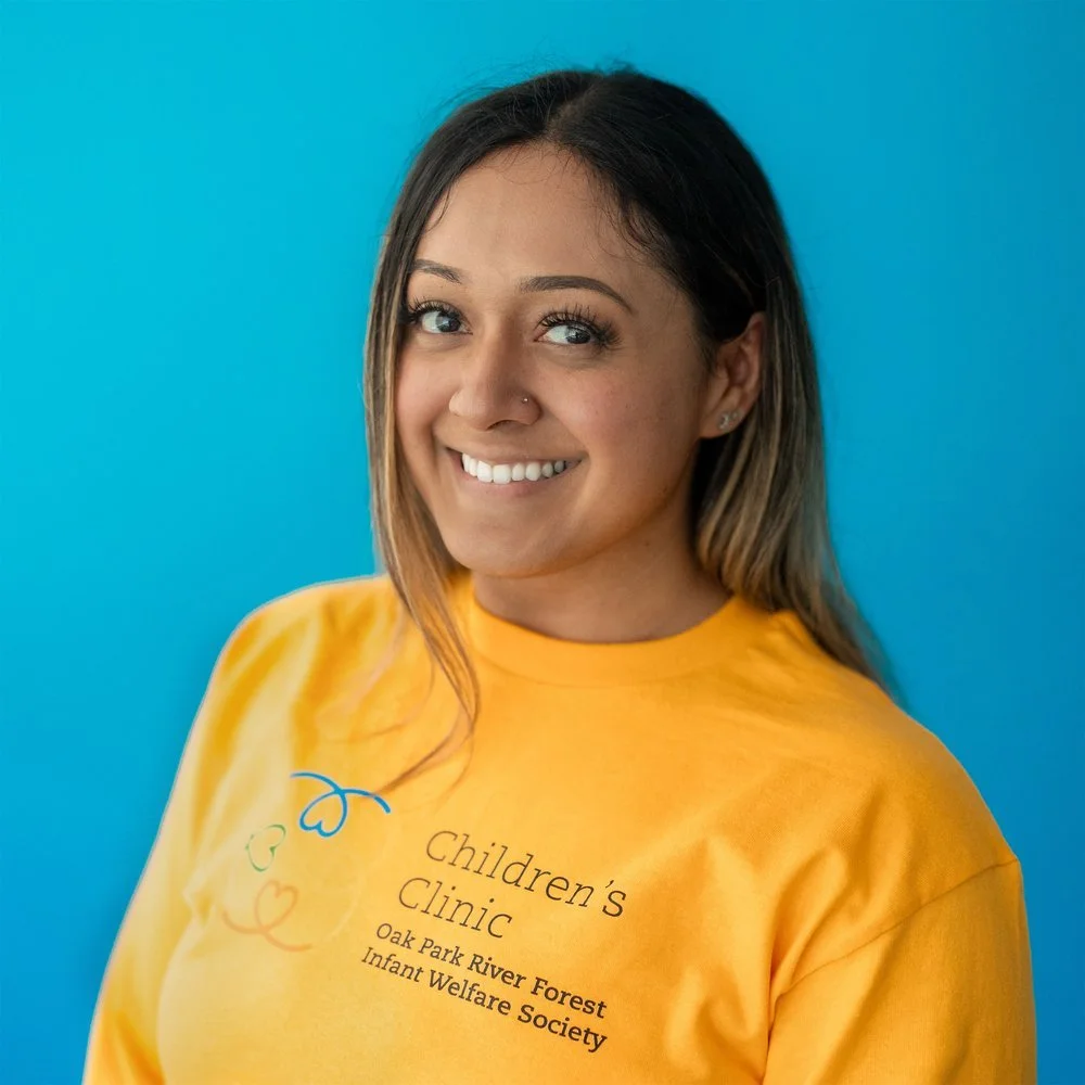 Person smiling, wearing a yellow shirt with 'Children's Clinic Oak Park River Forest Infant Welfare Society' text, set against a blue background.