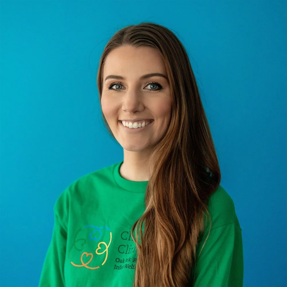 Smiling person wearing a green shirt with a logo, standing against a blue background.