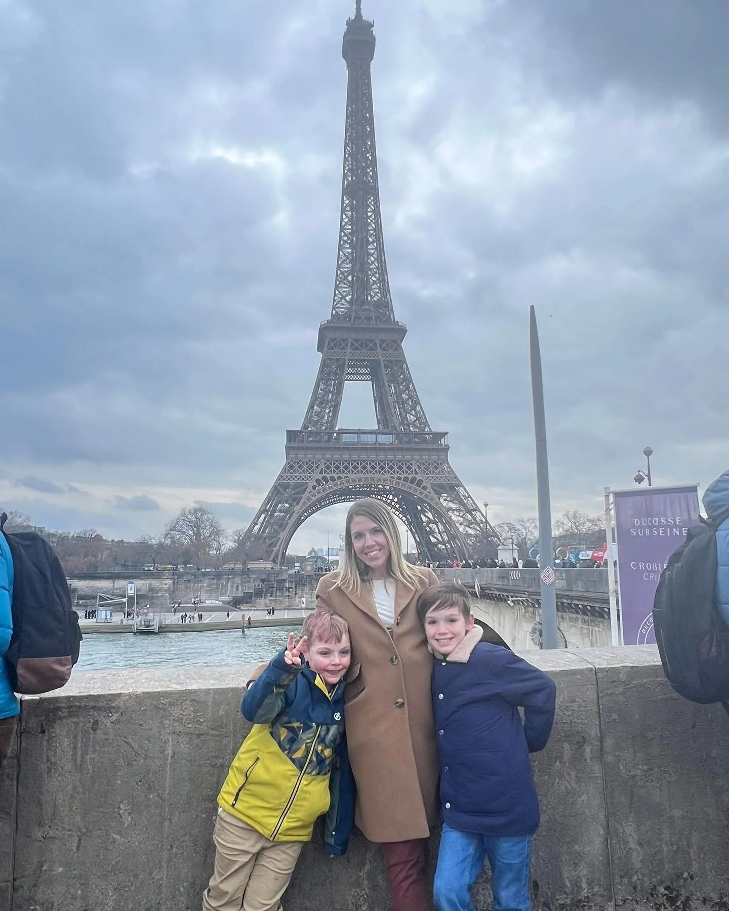 A woman and two children standing in front of the Eiffel Tower in Paris on a cloudy day.