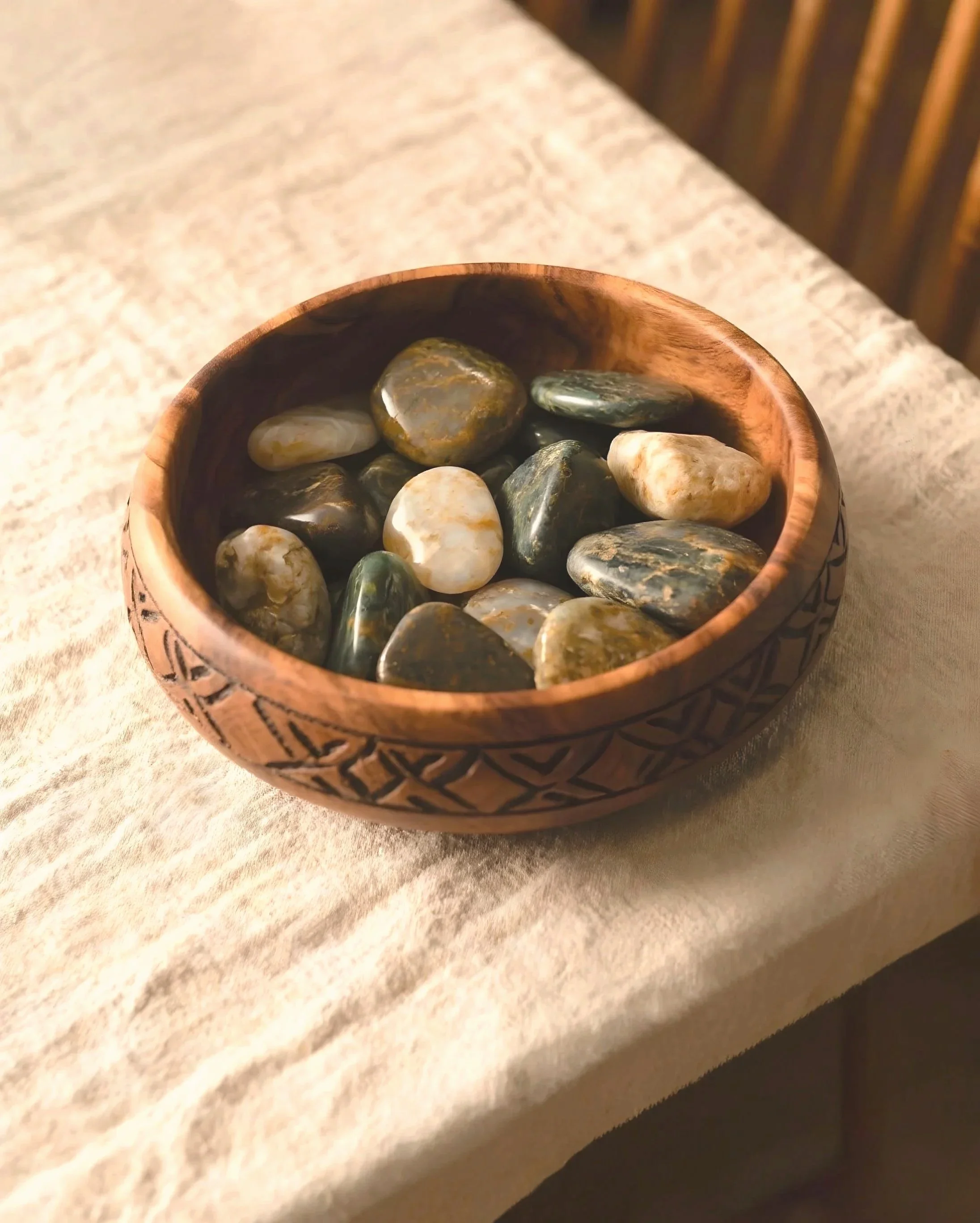 A wooden bowl filled with smooth, multicolored stones placed on a beige fabric surface. Used for creative, nature-based, therapy.