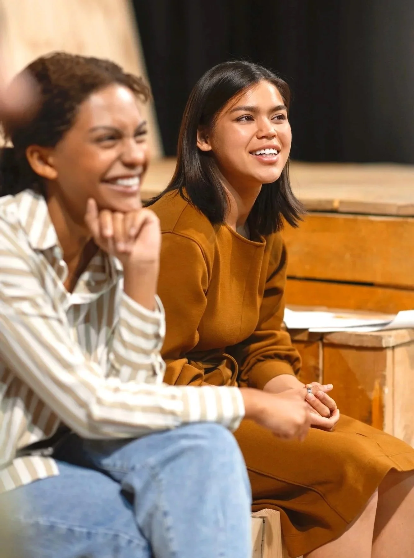 Two women sitting on a stage, smiling and engaging in conversation.
