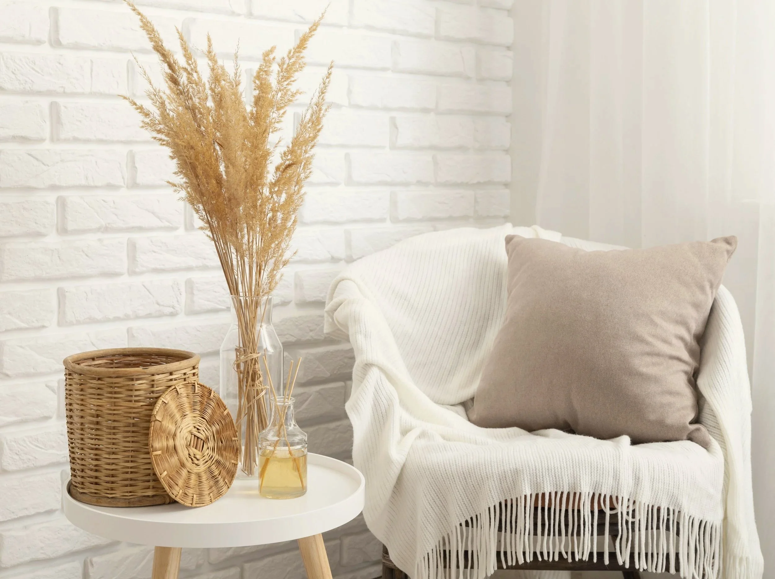 Decorative room with a white brick wall, a white armchair with a beige pillow, a white throw blanket, and a small round table holding wicker. A counselling therapy room, modern, cosy for private clients.