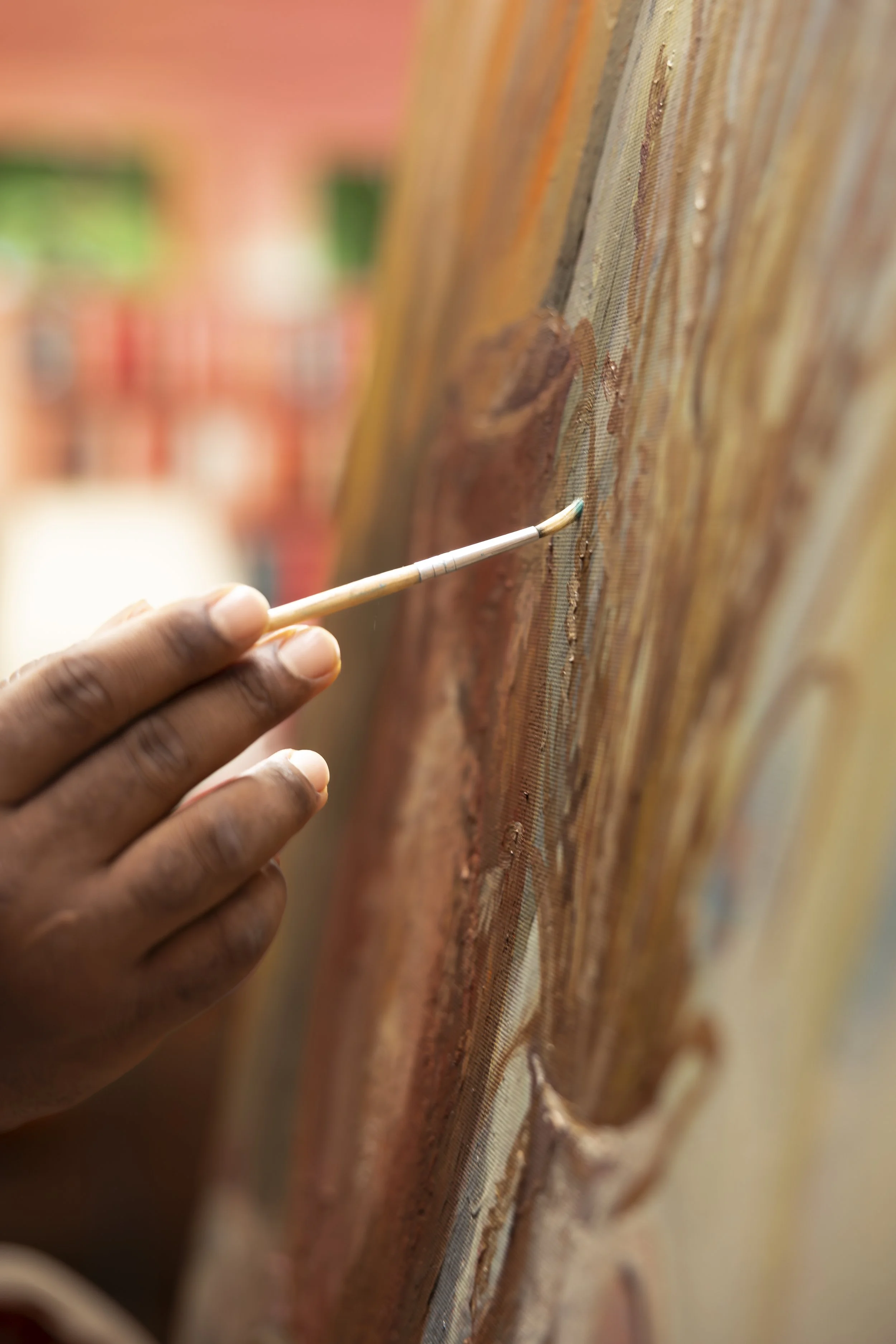 Close-up of a hand holding a paintbrush, painting on a large canvas with abstract brown, orange, and beige strokes. Art therapy.
