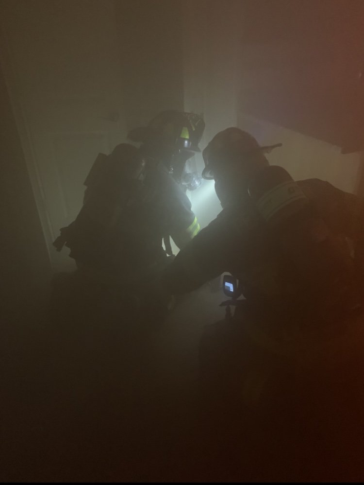 Two firefighters making their way trough a dark, smoky room.