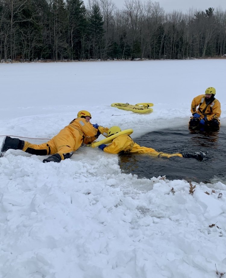 3 firefighters practice pulling someone out of the icy water in the winter.