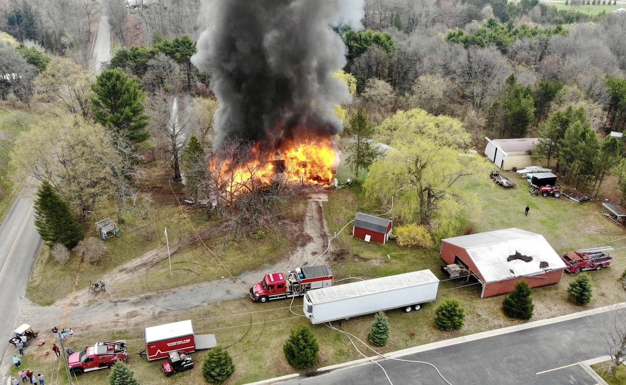 An arial view of a house burning, with multiple fire engines spraying water to put it out.