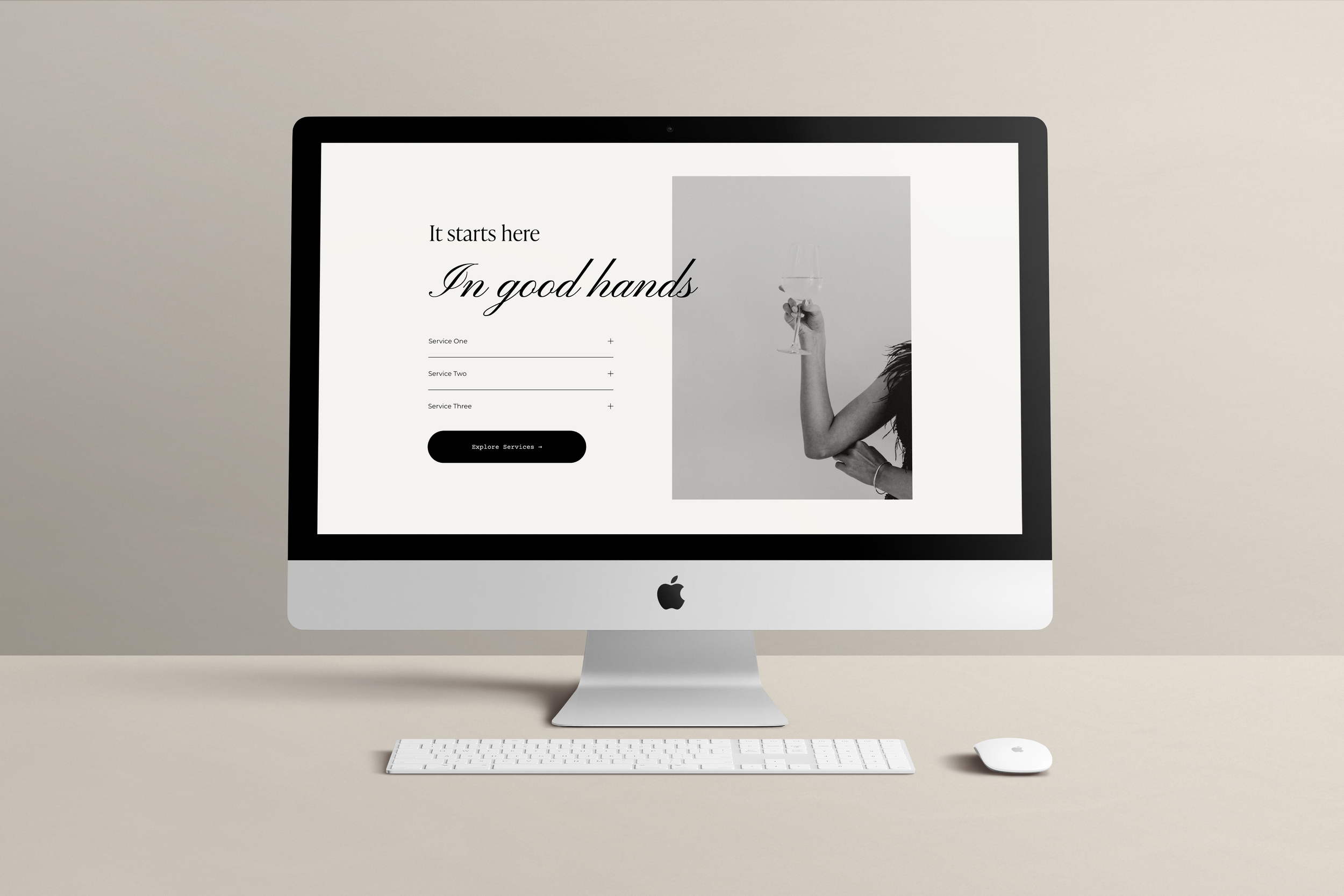 An Apple iMac computer on a desk displaying a website with the text 'It starts here, In good hands' and a black and white photo of a woman holding a wine glass.