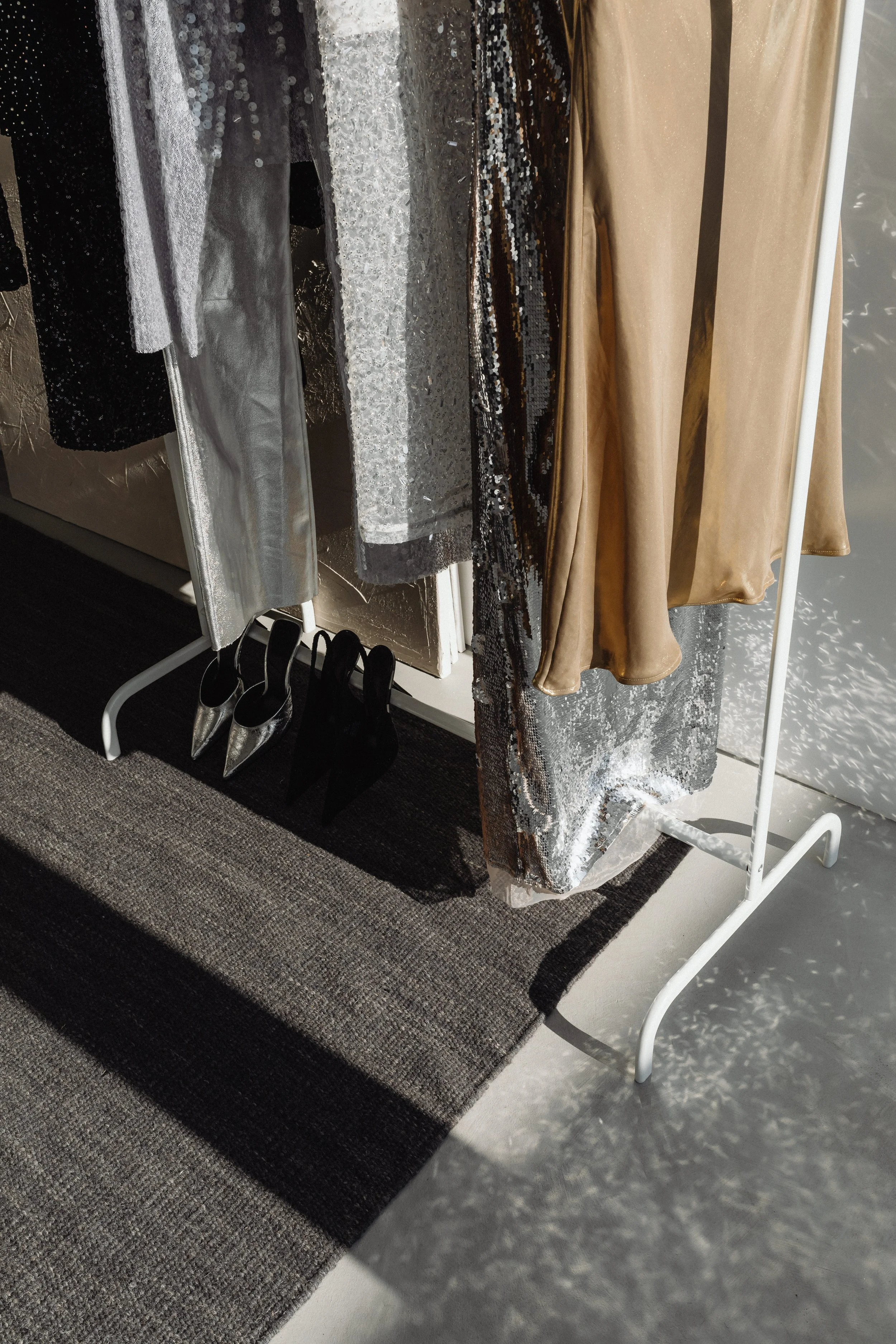 Clothing rack with dresses, shoes underneath, and a rug on the floor near the rack.