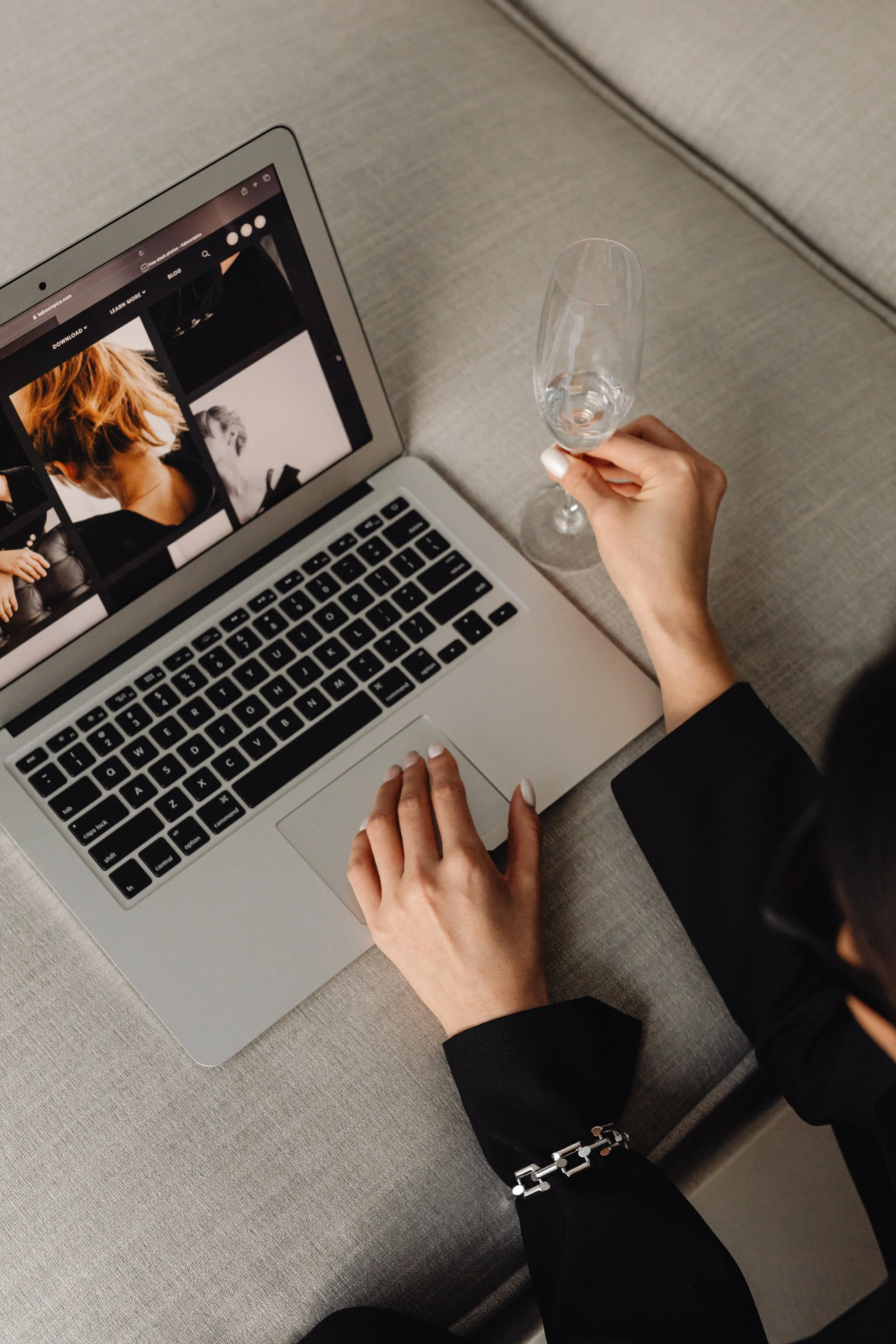 A woman browsing images on a laptop while holding a wine glass.