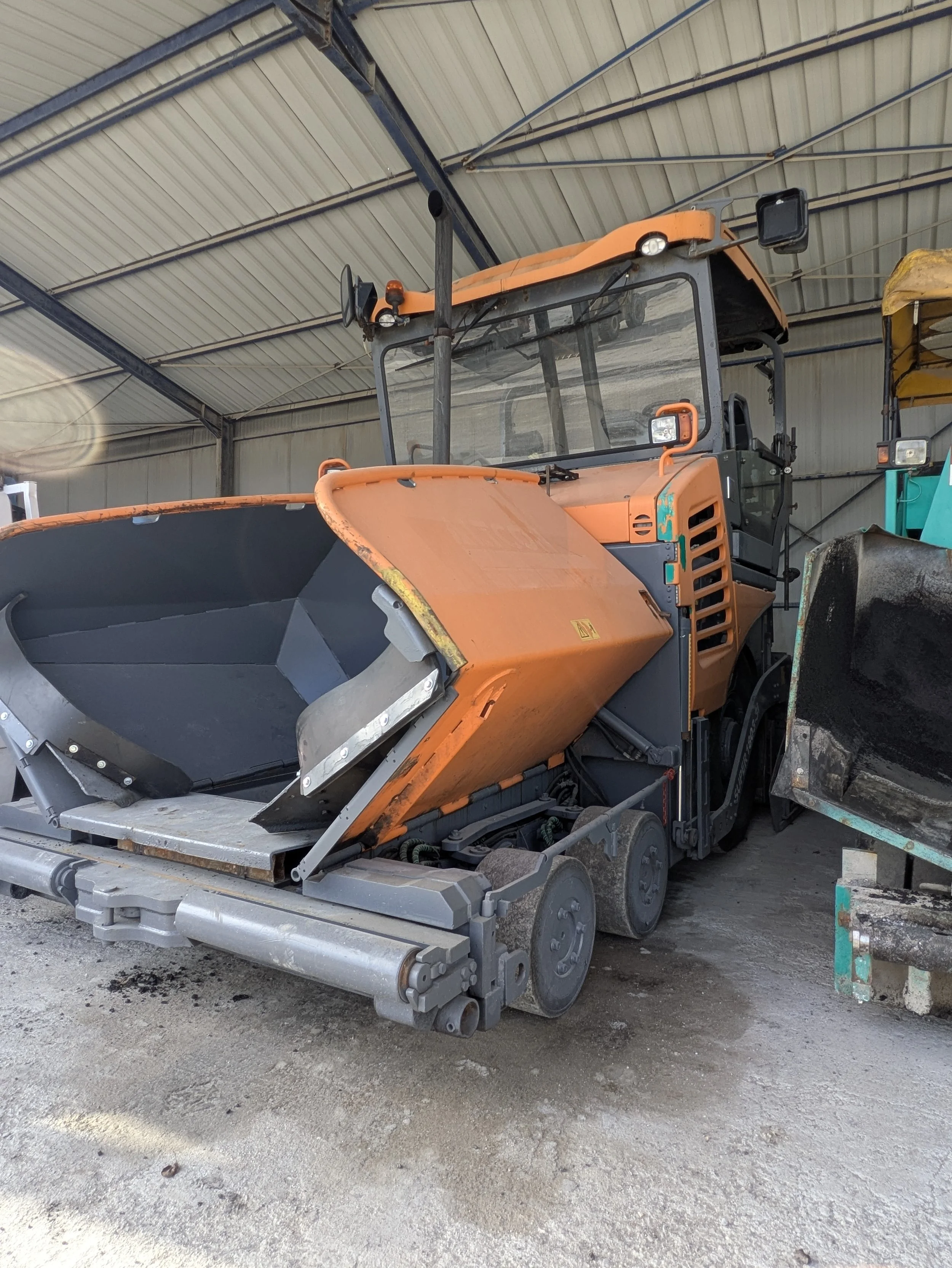 A large orange and gray street sweeping machine parked inside a storage facility.