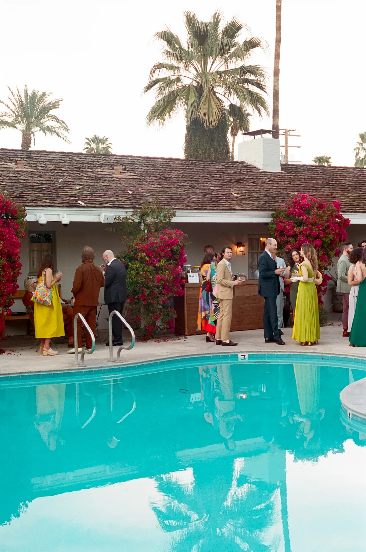 Candid 35mm film photo of wedding guests mingling at a poolside welcome party in Palm Springs. Documentary photography for multi-day wedding weekends.