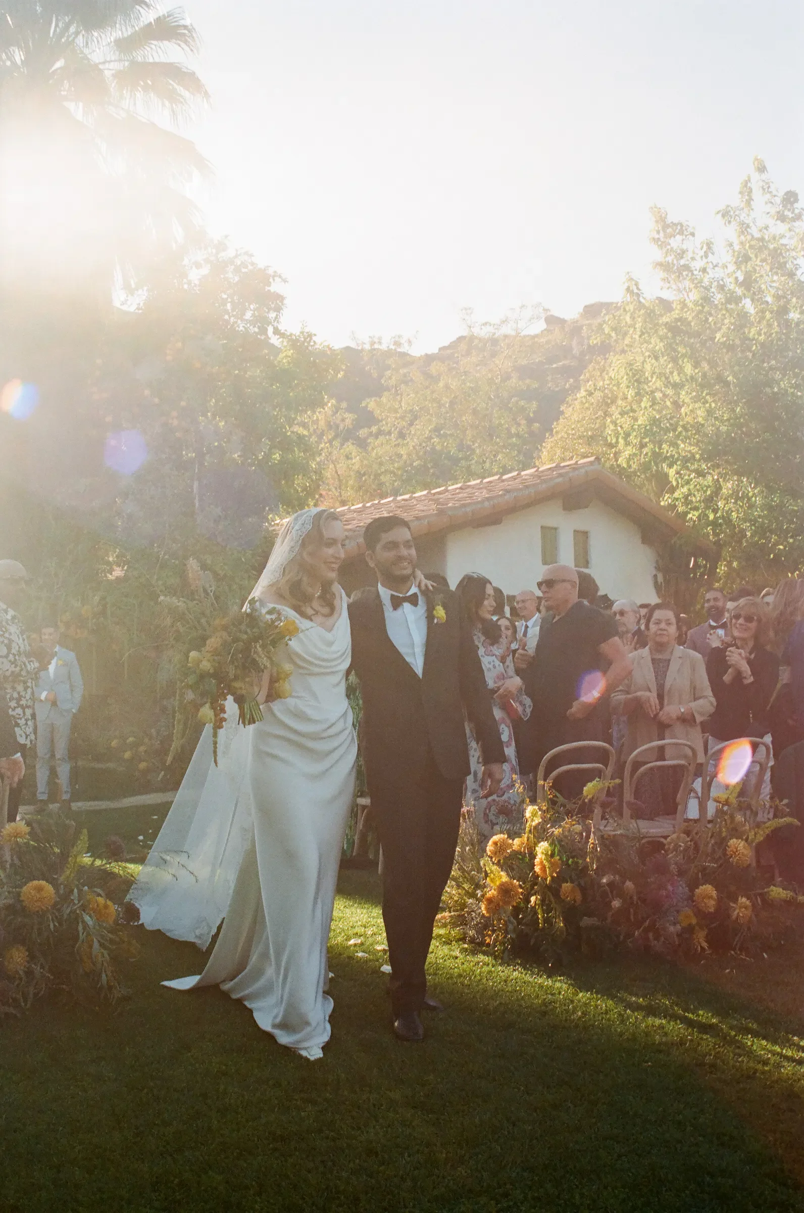 Ally and Abdullah just married walking down aisle at Casa Cody Palm Springs weekend wedding ceremony with golden hour sunlight and guests celebrating shot on 35mm film